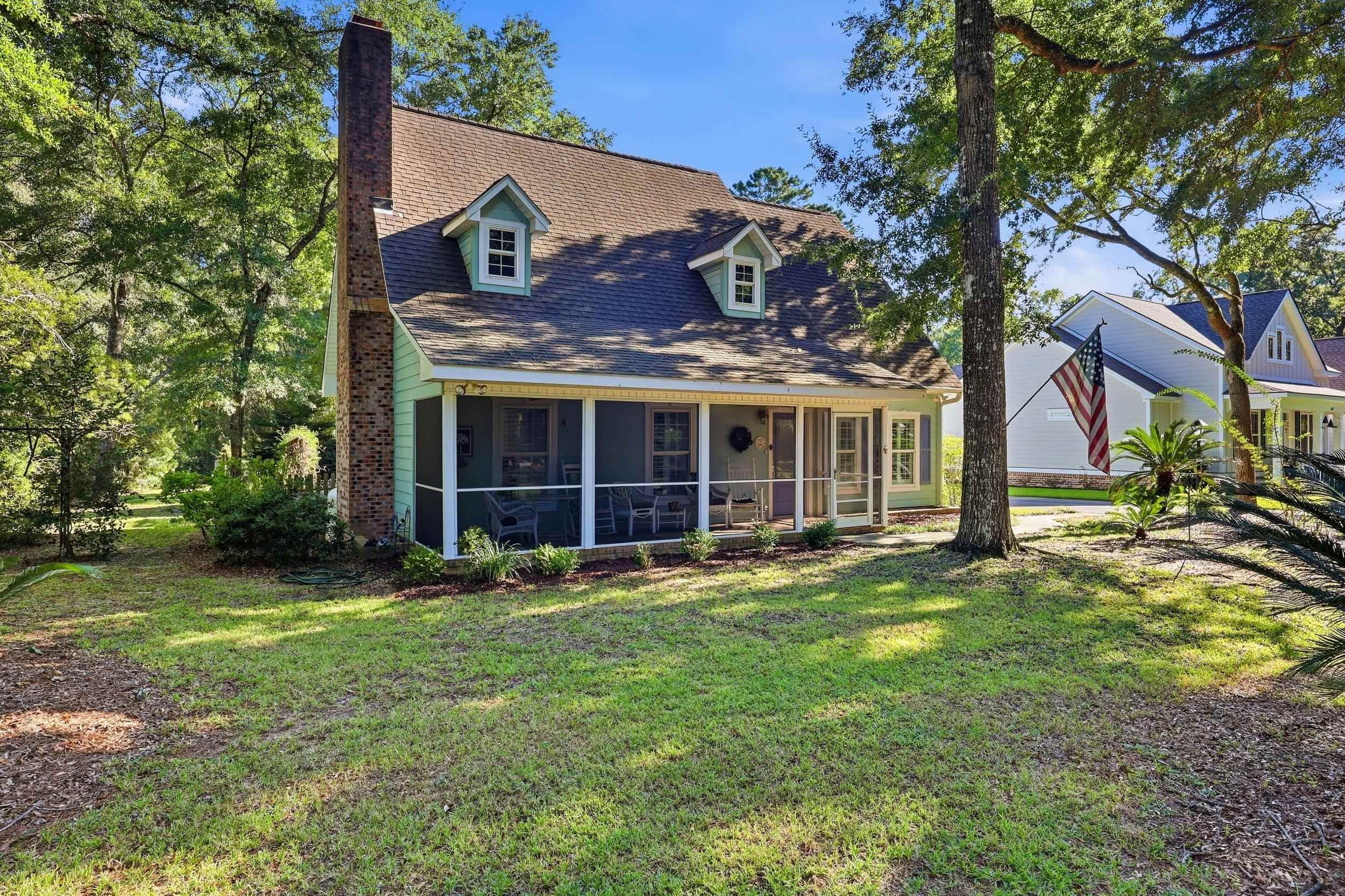 Two-story house with a screened porch, brick chimney, and mature trees surrounding a grassy yard.