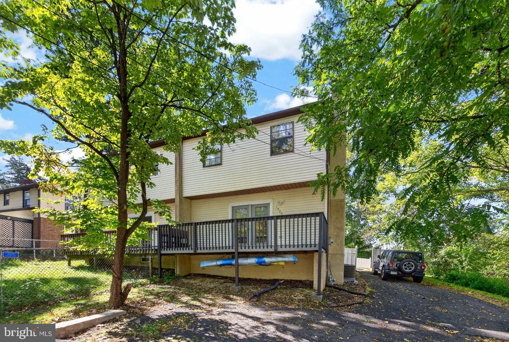Home’s rear exterior with a raised deck, mature trees, and a driveway