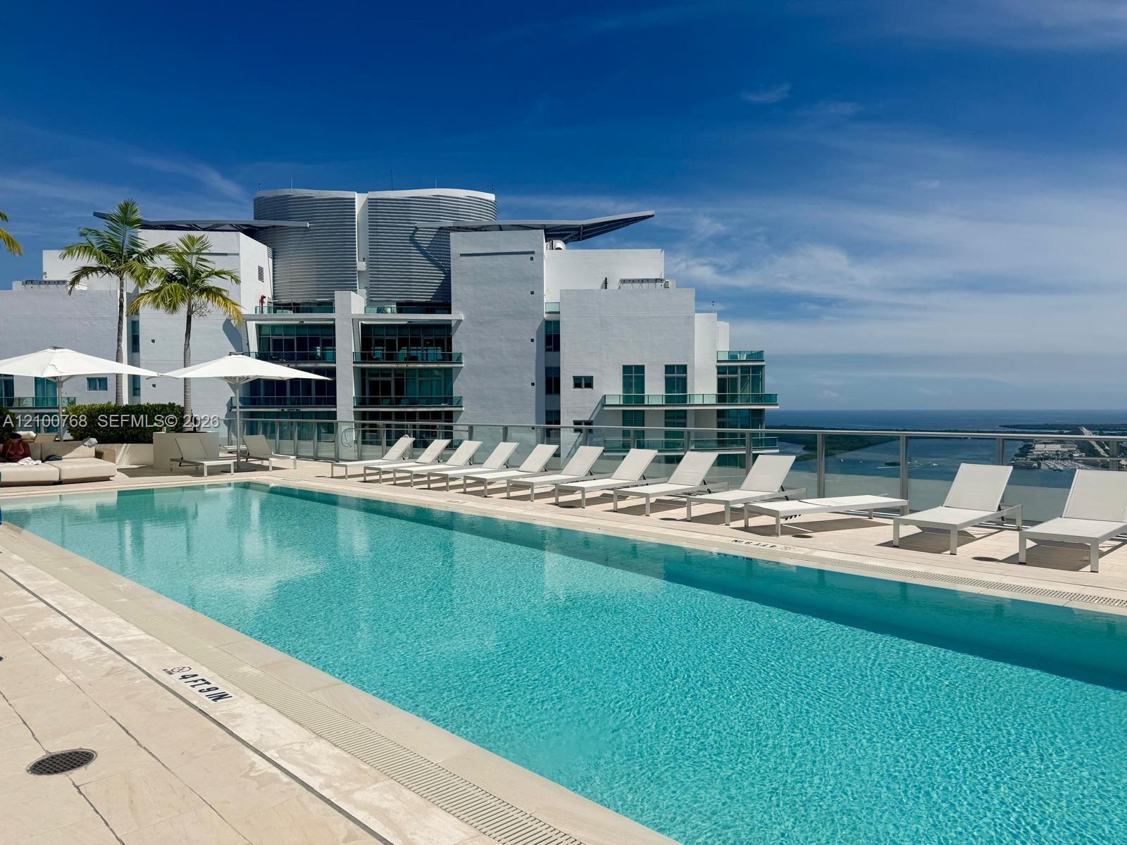 Rooftop pool beside a modern high-rise, lined with white loungers and overlooking the bay.