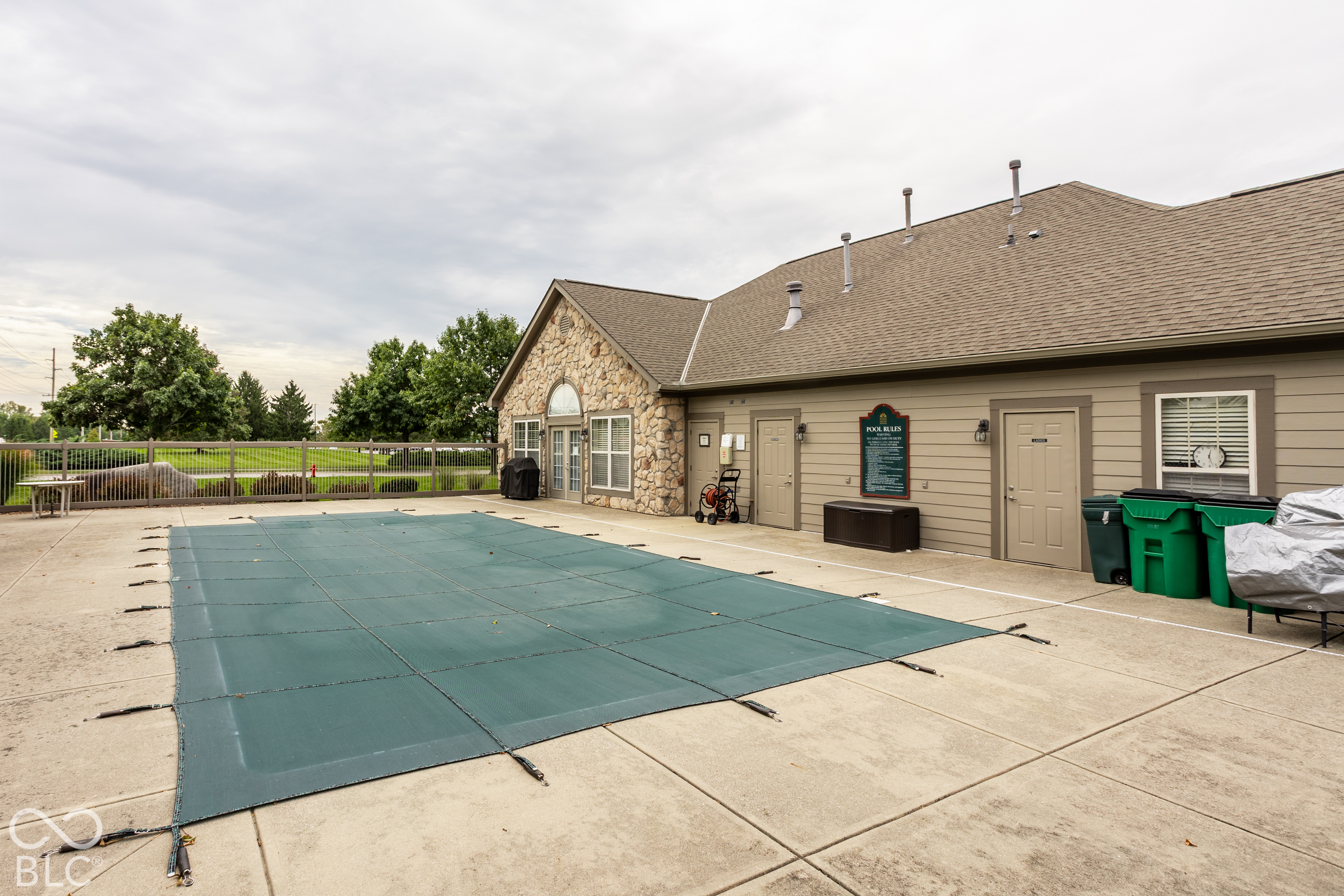Community pool covered with a green safety cover beside a stone-accented clubhouse.