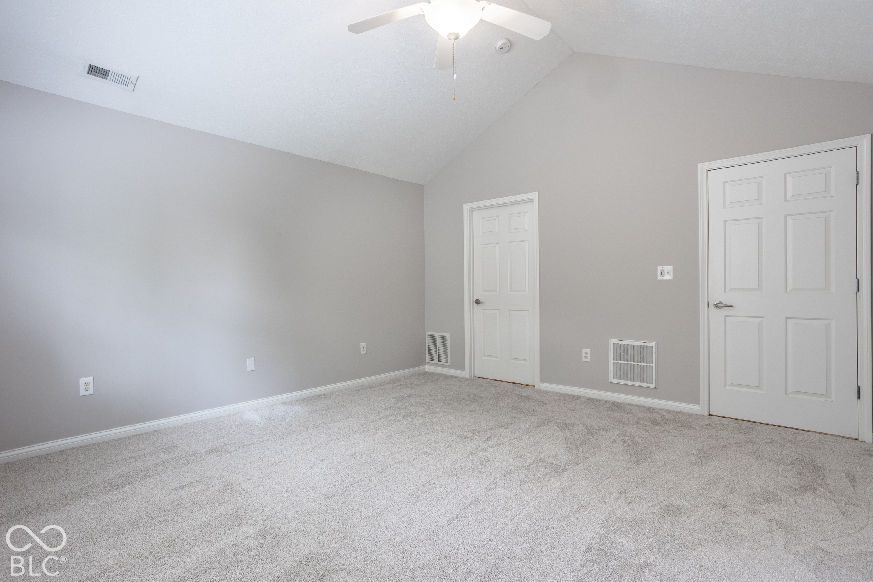Empty carpeted room with a vaulted ceiling, ceiling fan, and two white doors.