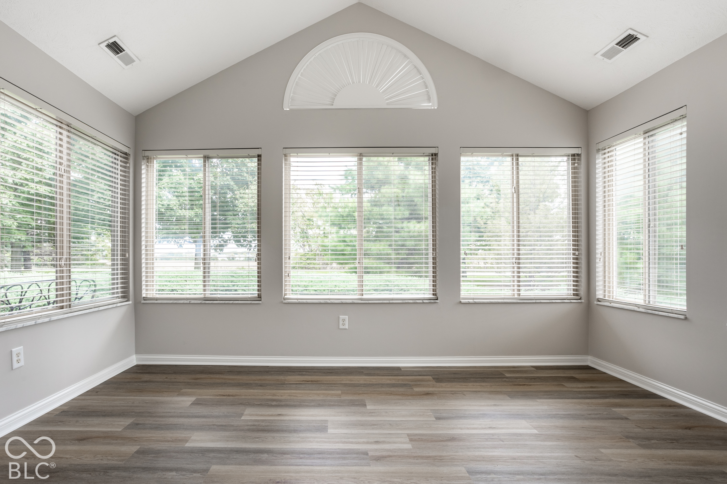 Empty room with windows on three sides, white blinds, and a semicircular fanlight above the center windows.