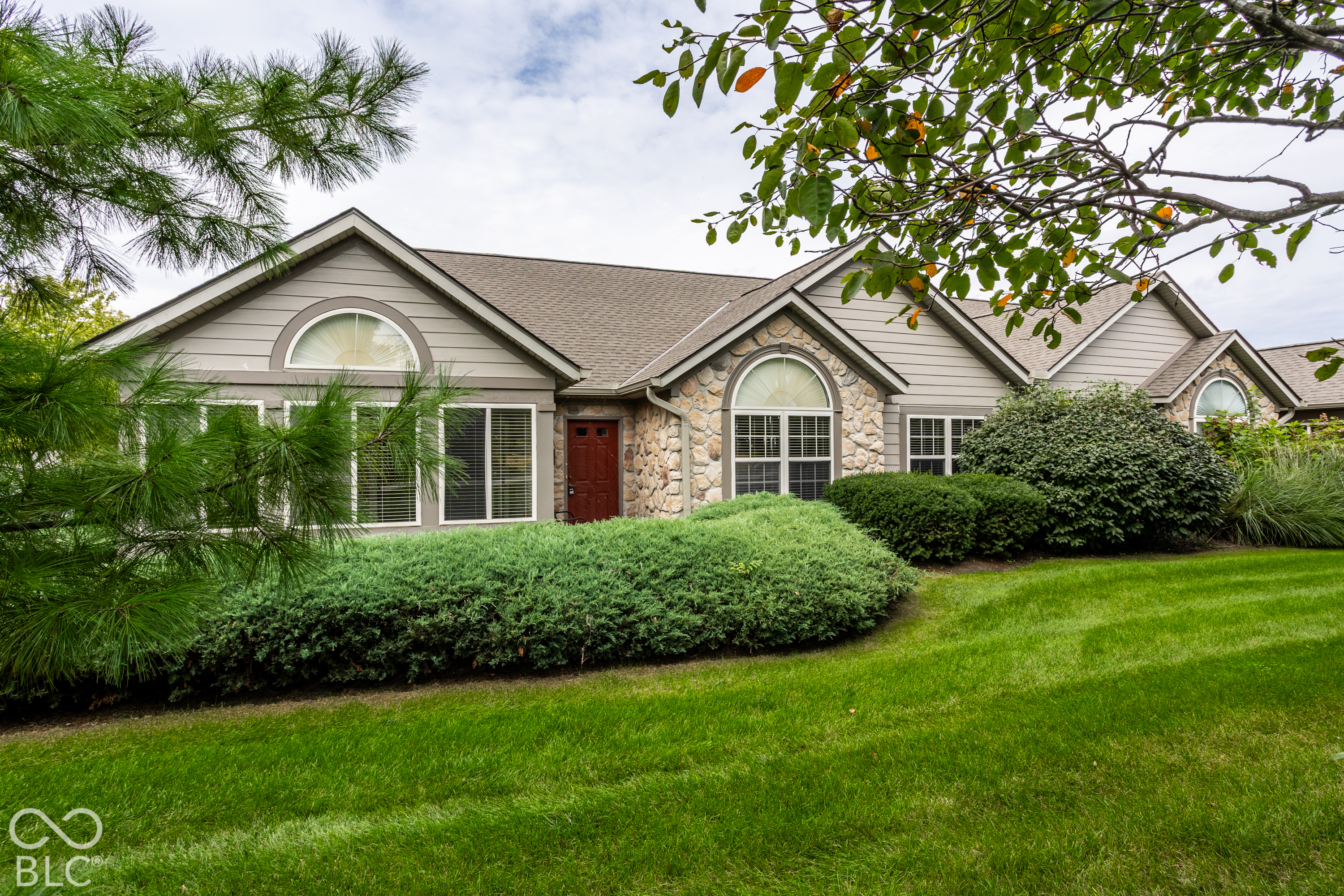 Single-story home with a stone facade, arched windows, red door, and landscaped lawn.