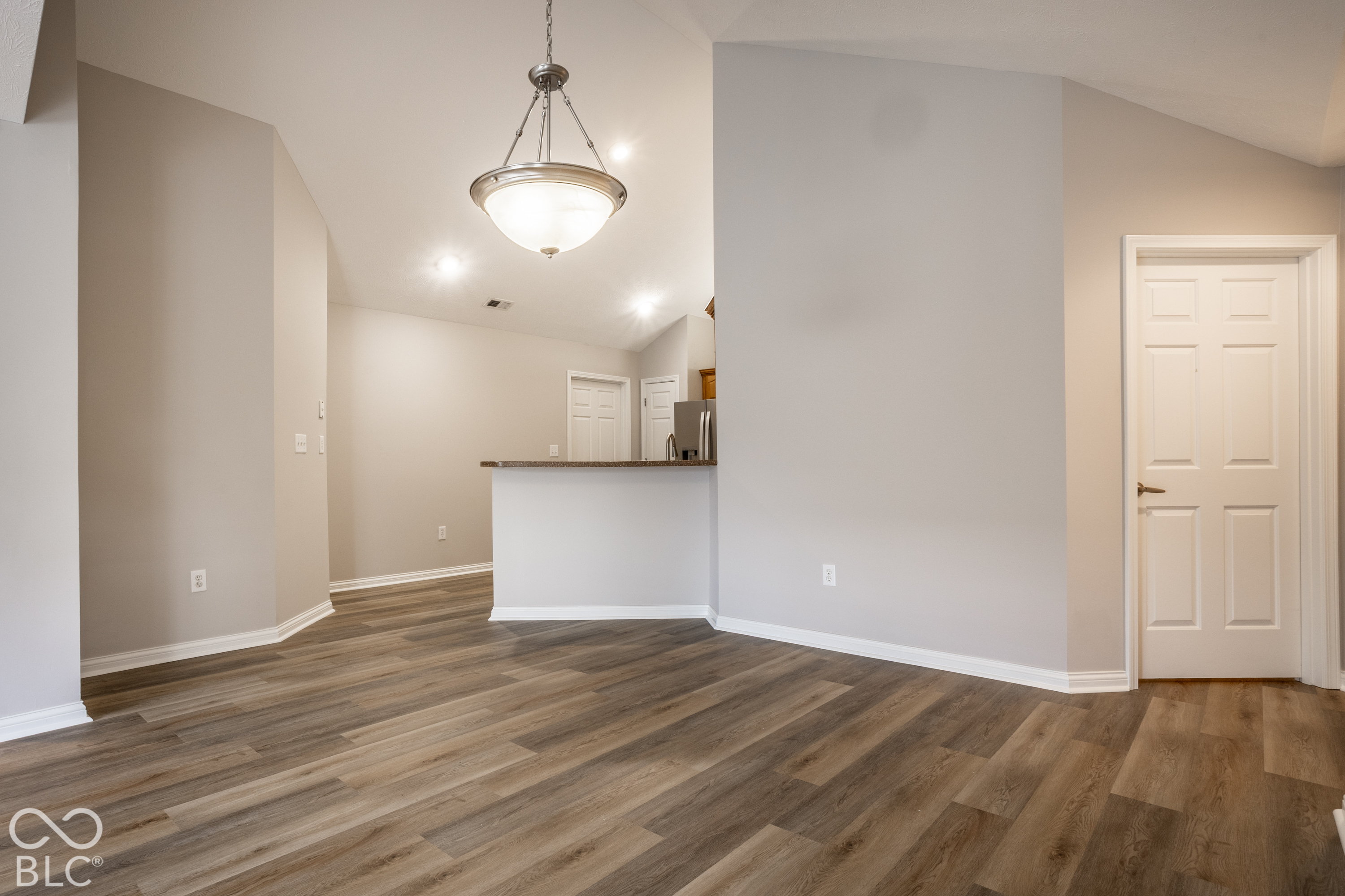Empty dining area with wood-look floors, pendant light, and breakfast bar opening to the kitchen.