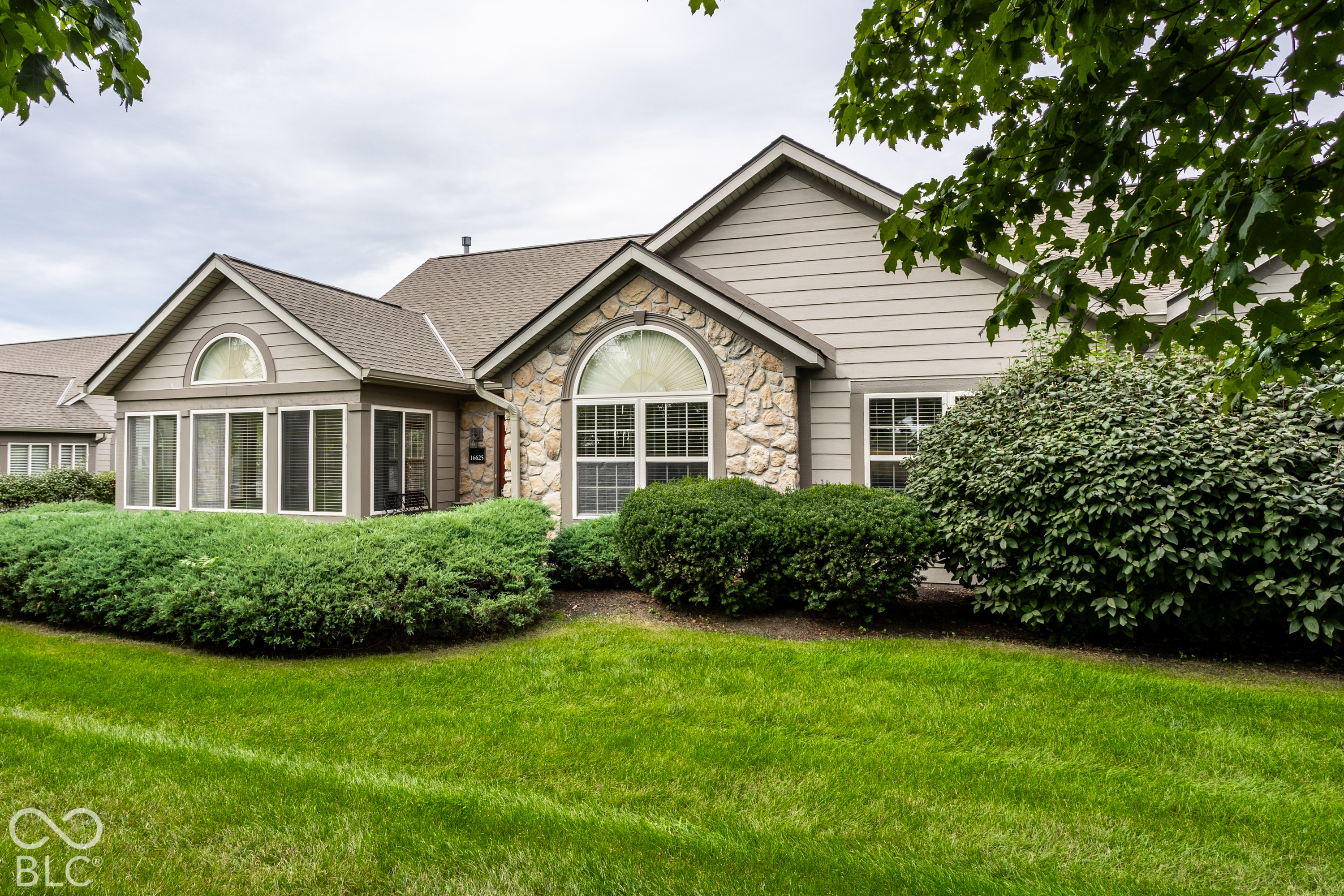 Home exterior with a stone facade, arched windows, and neatly trimmed shrubs and lawn.