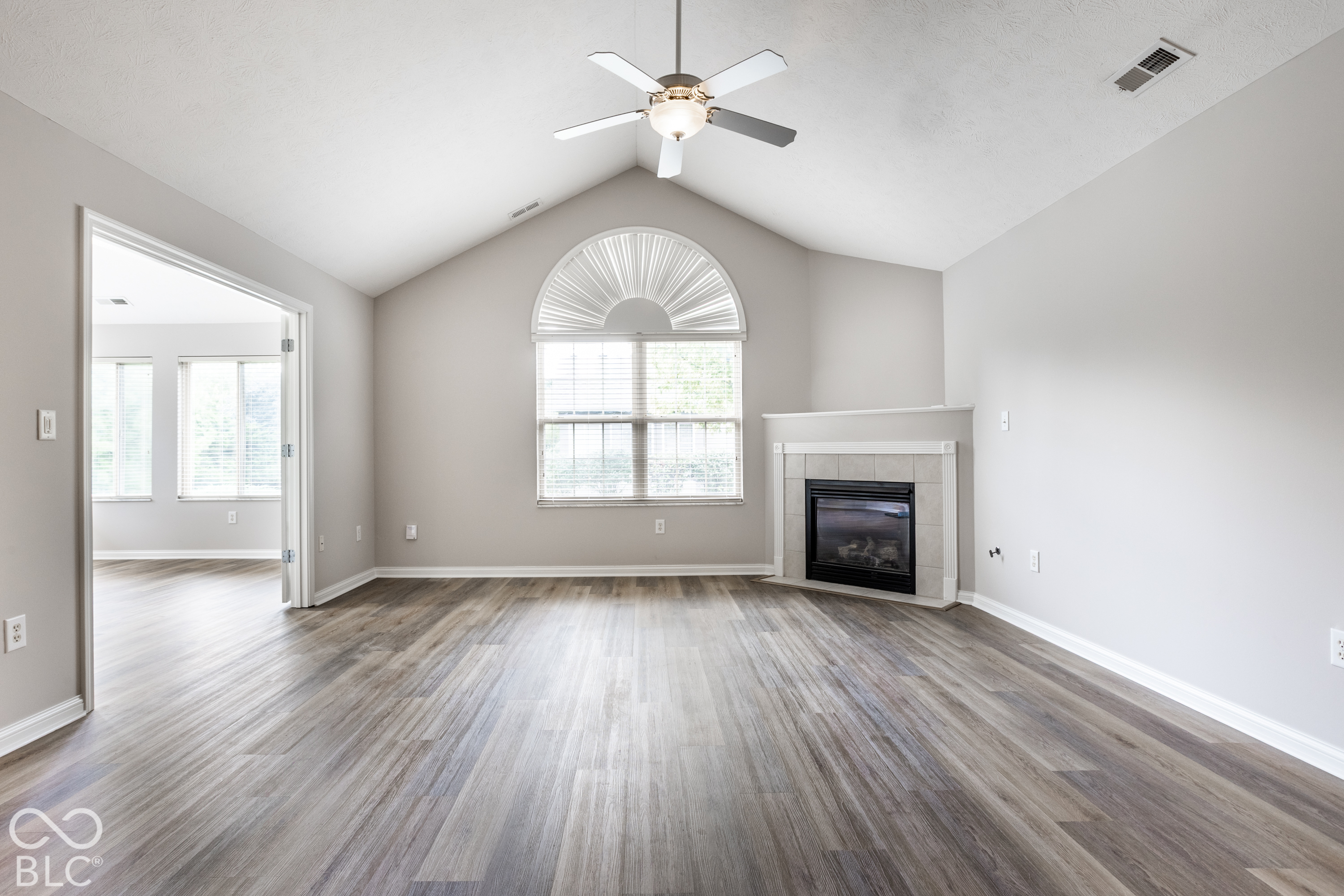Vacant living room with vaulted ceiling, arched window, gray flooring, and tiled fireplace.