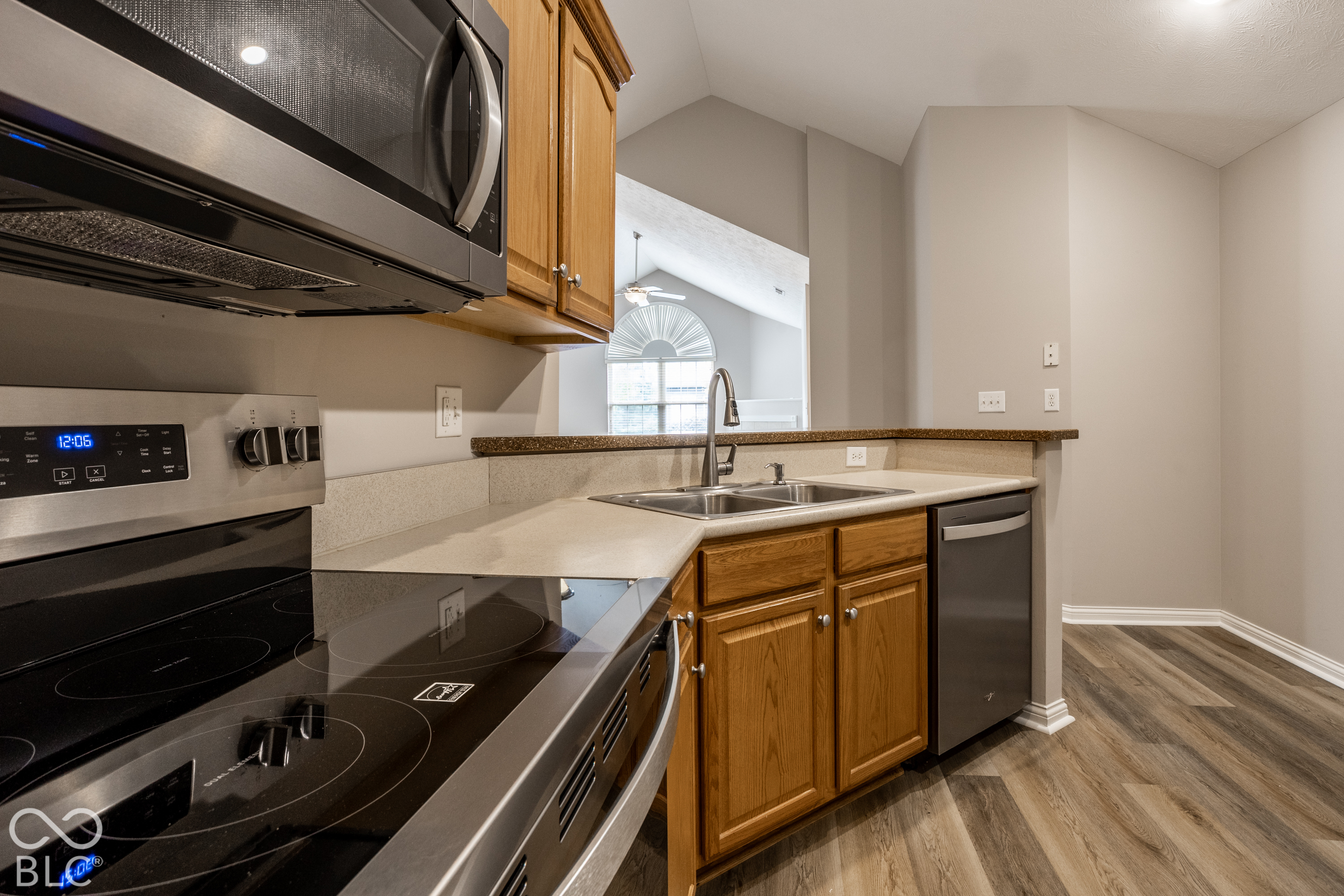 Kitchen with warm wood cabinets, stainless steel appliances, and a sink facing a bright room with an arched window.