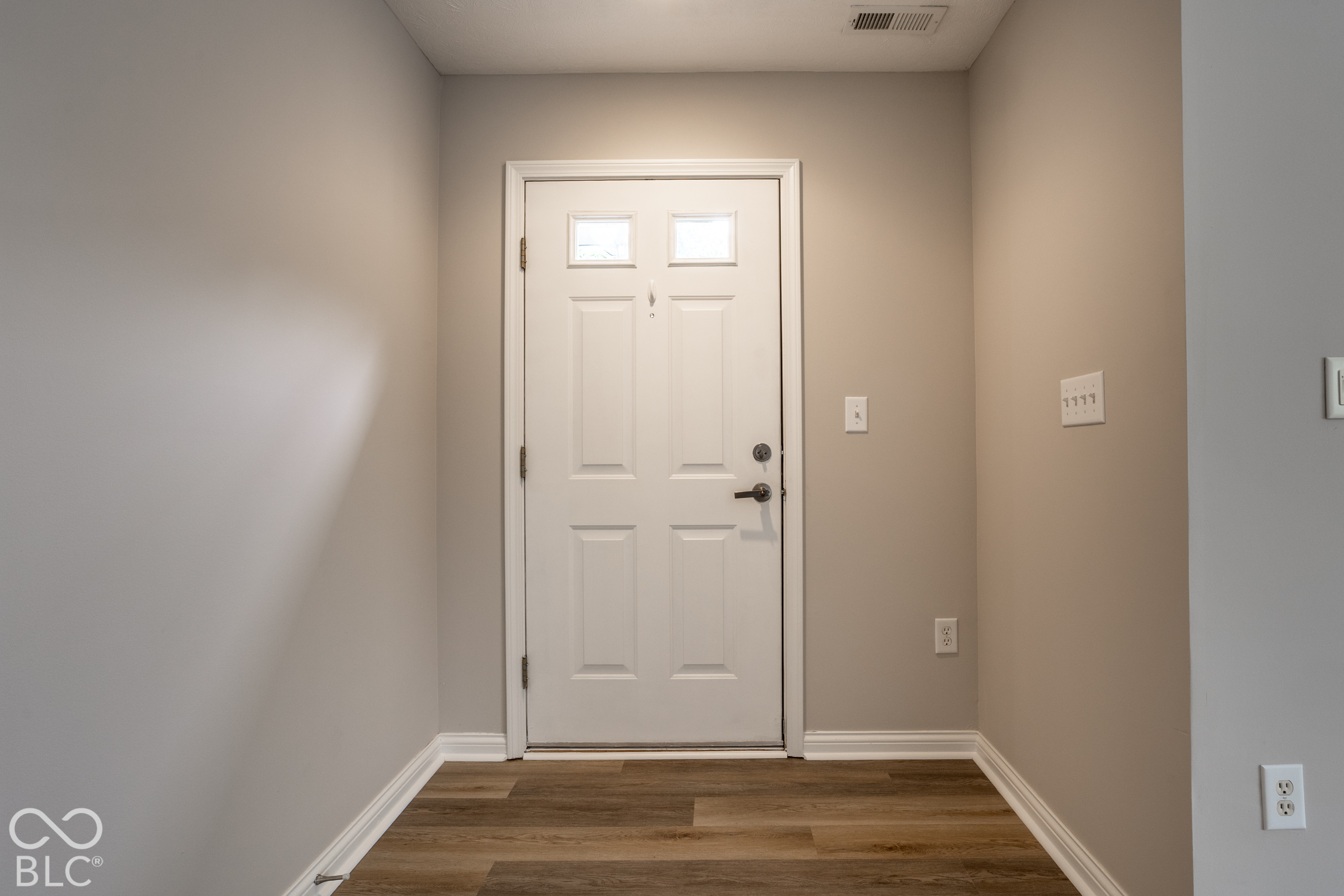Entryway with a white paneled front door and brown wood-look flooring.