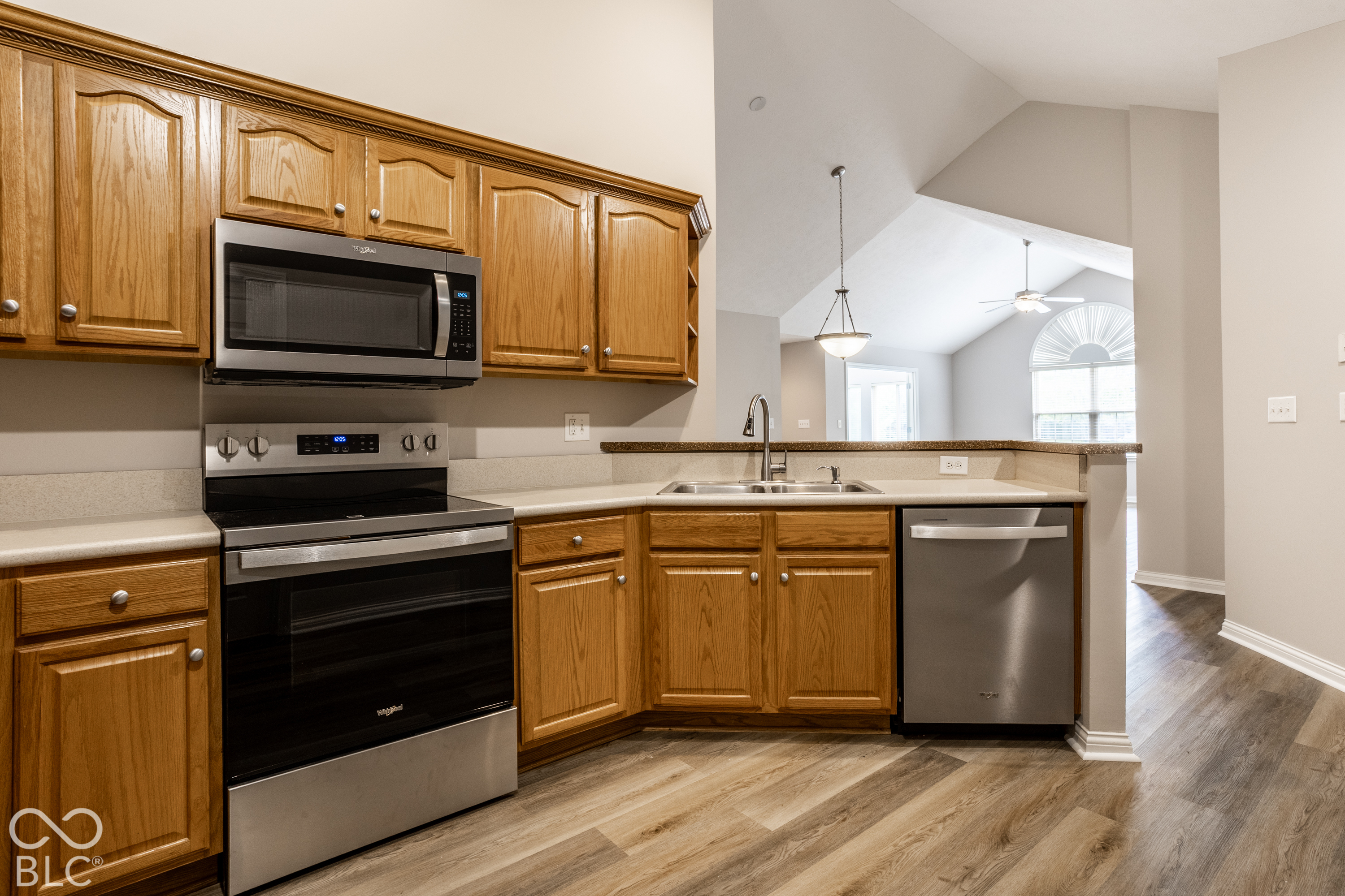 Kitchen with honey-toned wood cabinets, stainless steel appliances, and an open view into a vaulted living area.