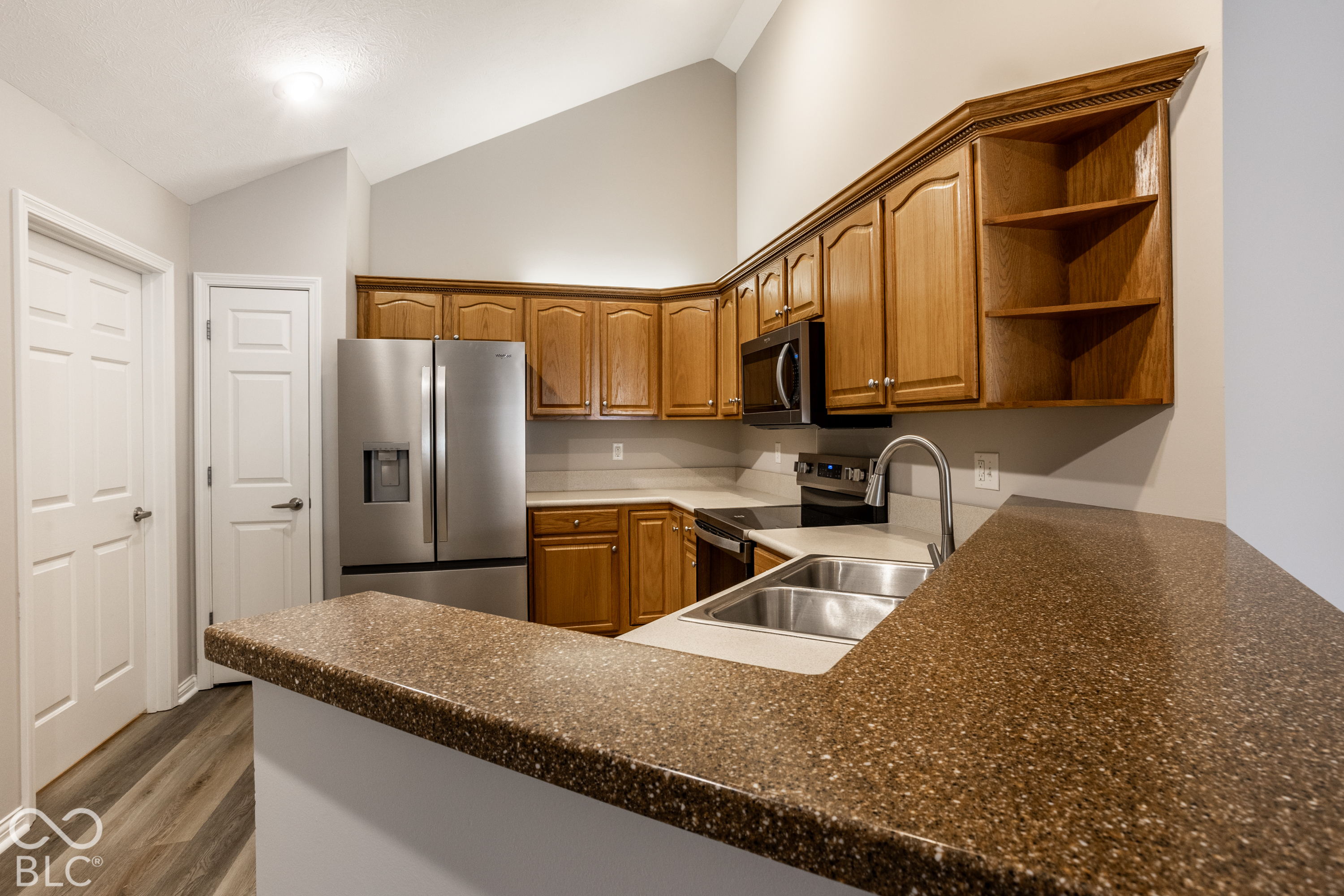 Kitchen with wood cabinets, stainless steel appliances, and a large speckled countertop peninsula.