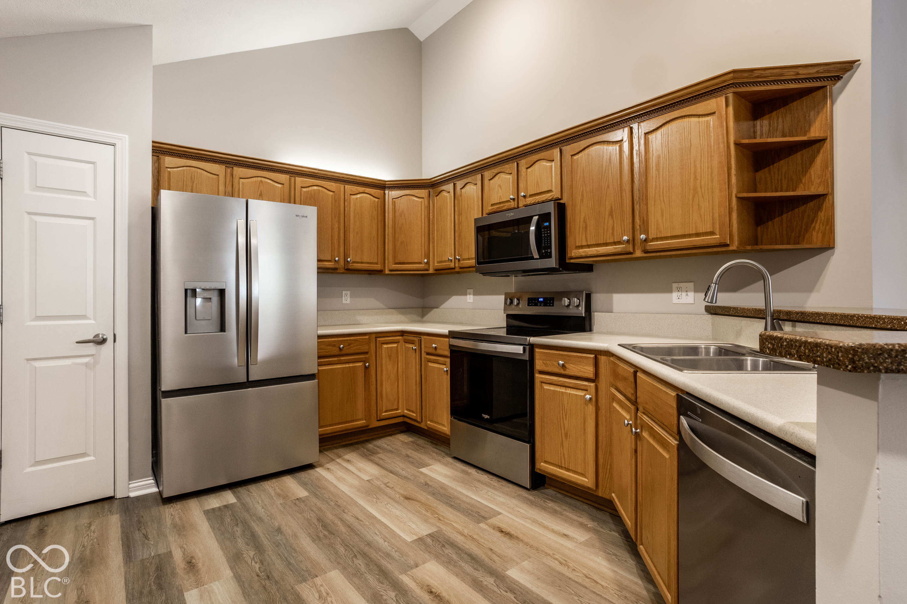 Kitchen with honey-colored cabinets, stainless steel appliances, light countertops, and wood-look flooring.