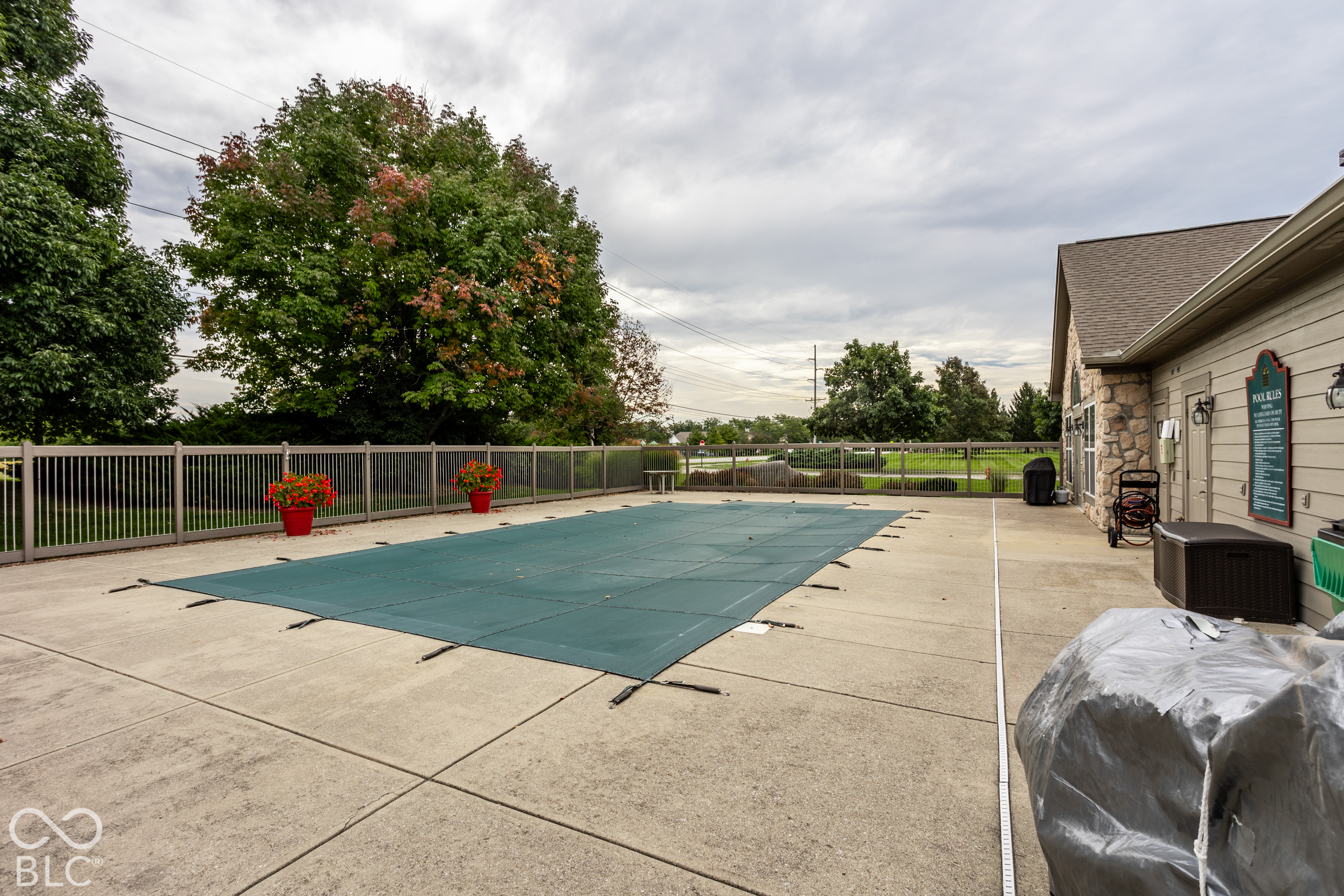 Covered outdoor pool beside a fenced concrete deck and stone-and-siding building.