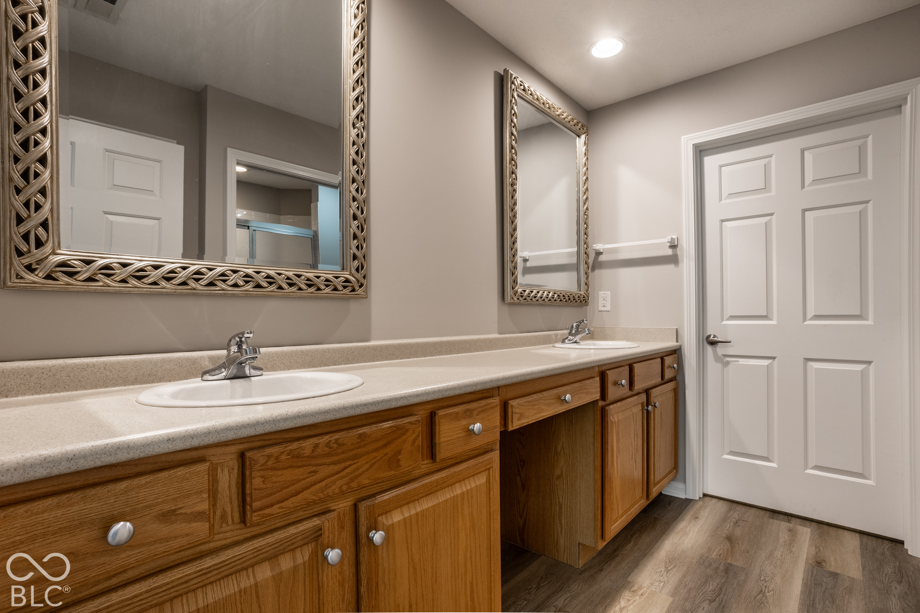 Bathroom double vanity with warm wood cabinets, ornate mirrors, and a light speckled countertop.