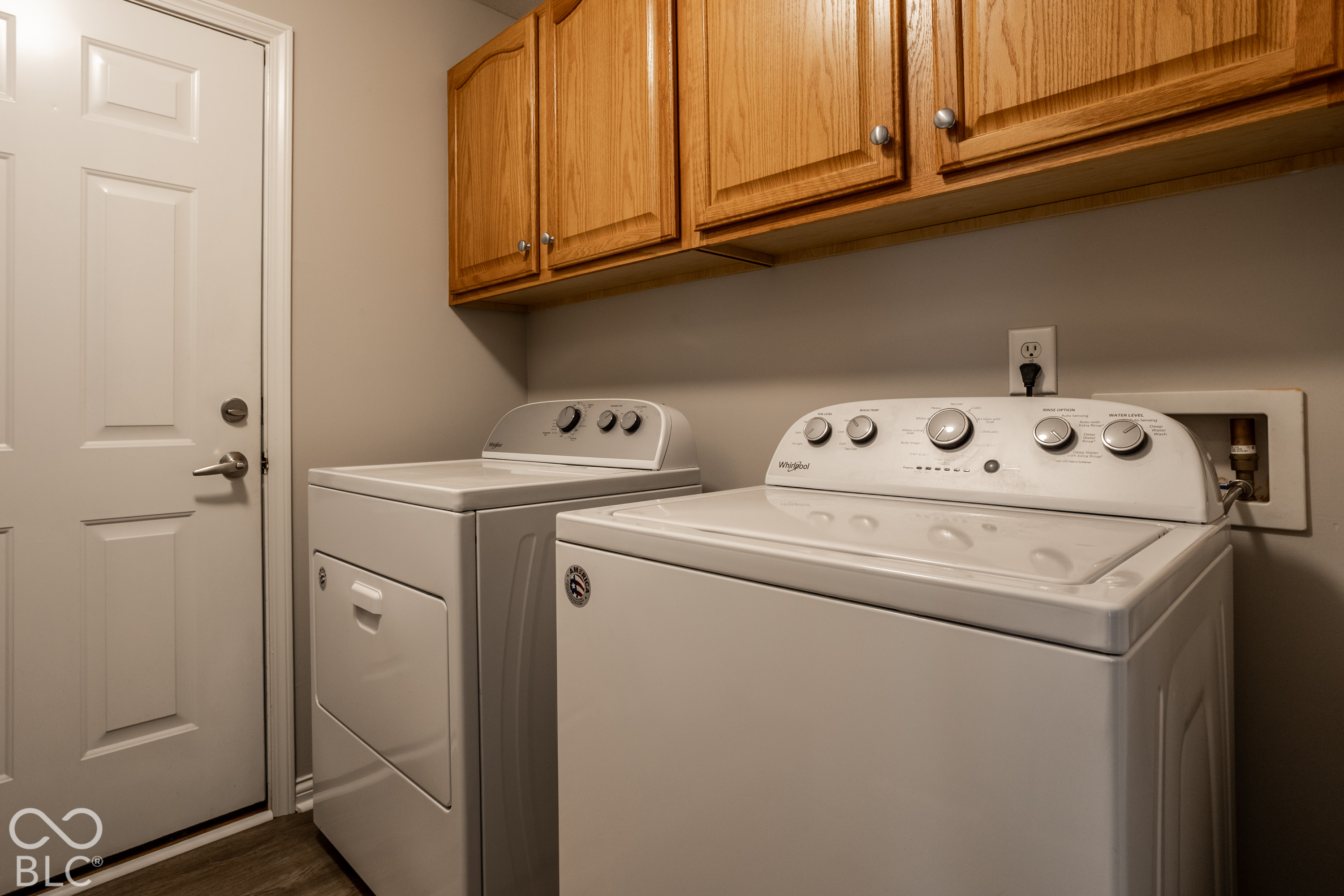 Laundry room with a white washer and dryer beneath wood cabinets.