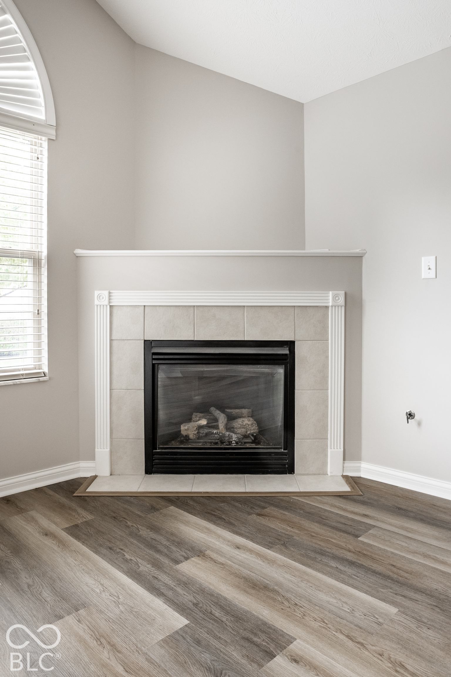 Tiled fireplace with a black insert beside a window with white blinds.