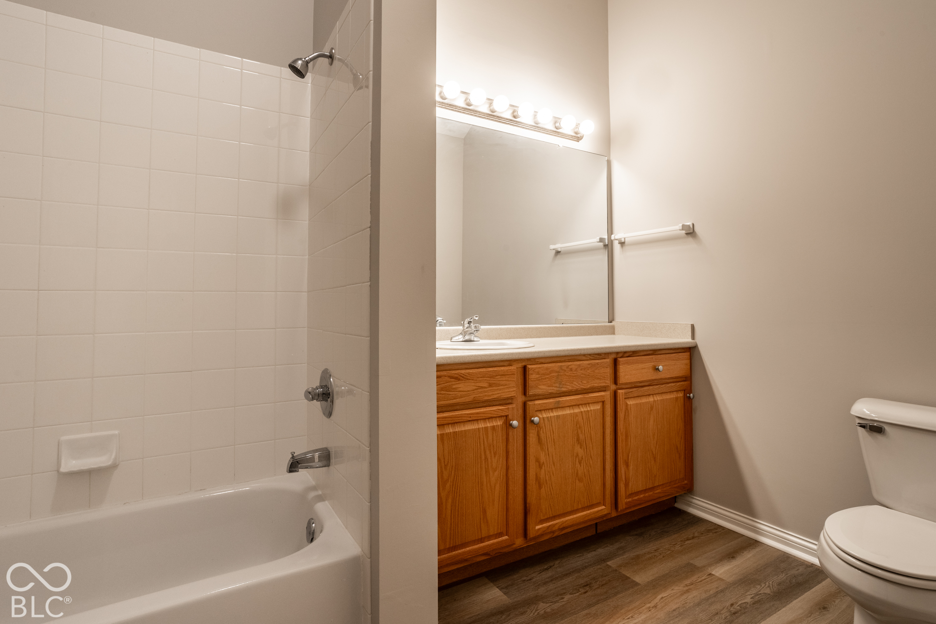 Bathroom with a tiled tub and shower beside a wood vanity and large mirror.