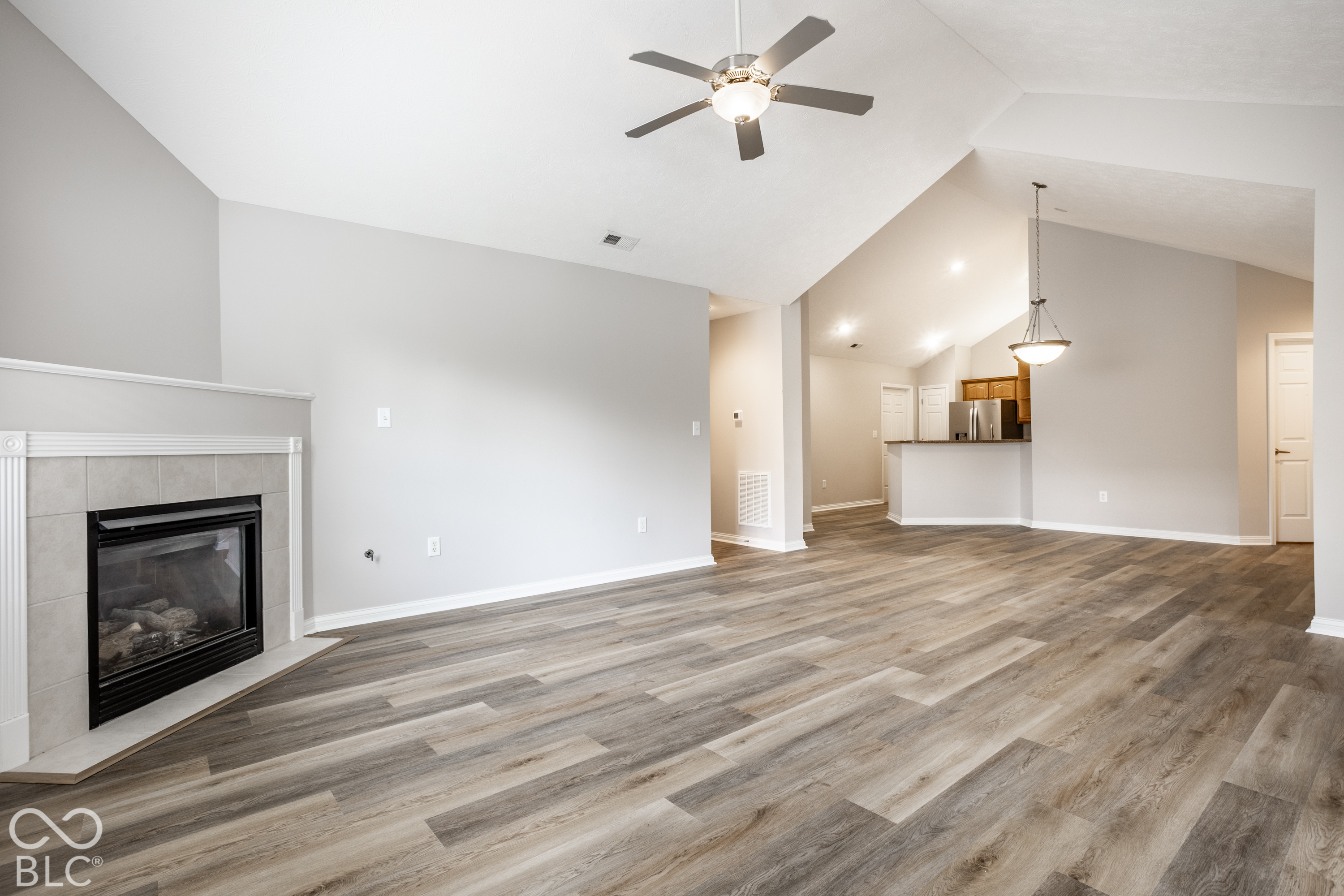 Unfurnished living room with a tiled fireplace and open view of the kitchen.