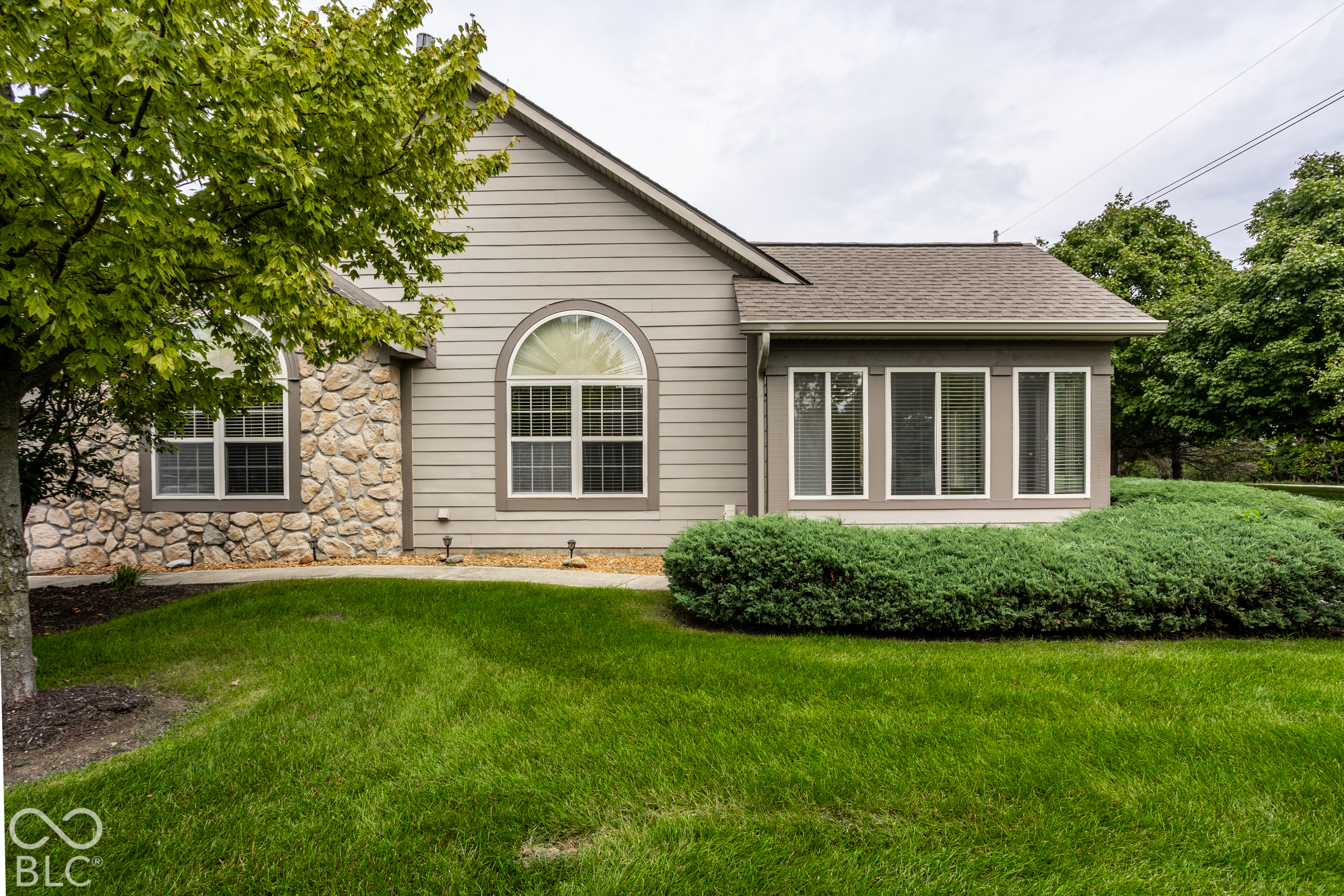 Gray house exterior with stone accents, an arched window, and a broad green lawn.