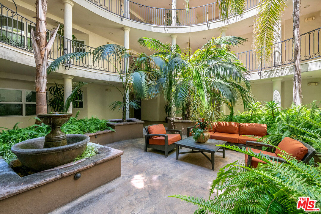 Residential courtyard with a stone fountain, palms, and orange outdoor seating.