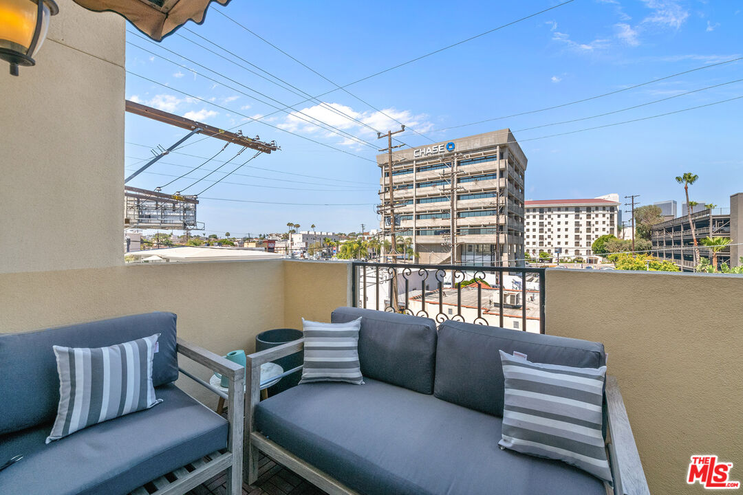 Furnished apartment balcony with gray seating overlooking an urban view and a Chase office building.