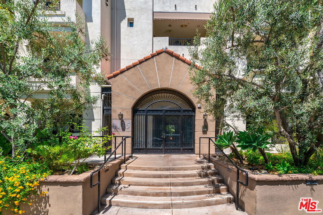 Residential building entrance with an arched tiled canopy, black gates, landscaped steps, and address 1135.
