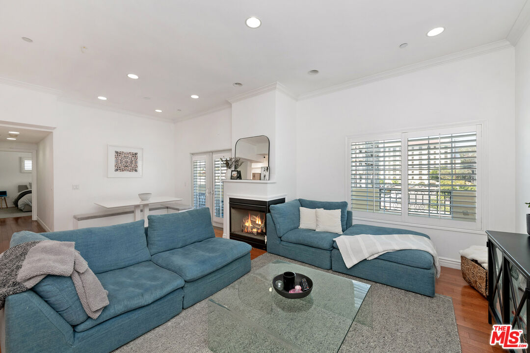 Living room with blue sectional sofas, a lit fireplace, and large windows overlooking neighboring buildings.