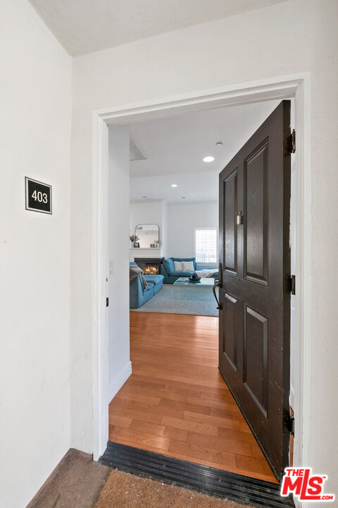 Apartment entryway with hardwood flooring, an open dark door, and a living room with blue seating beyond.