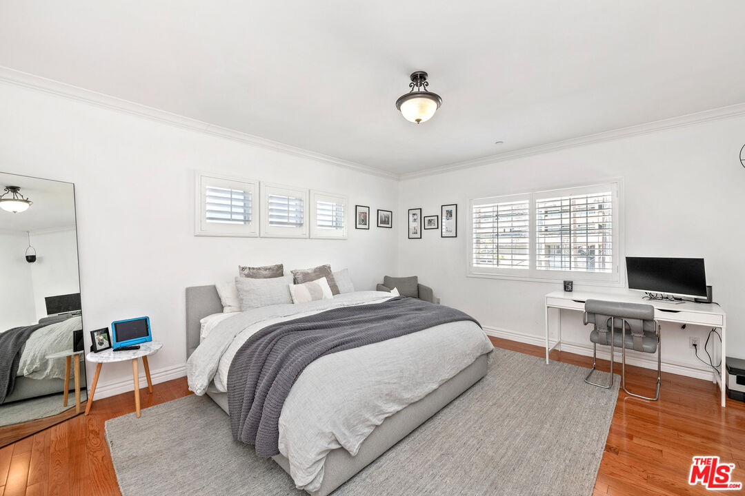 Bedroom with a large white-and-gray bed, hardwood floors, shuttered windows, and a desk.