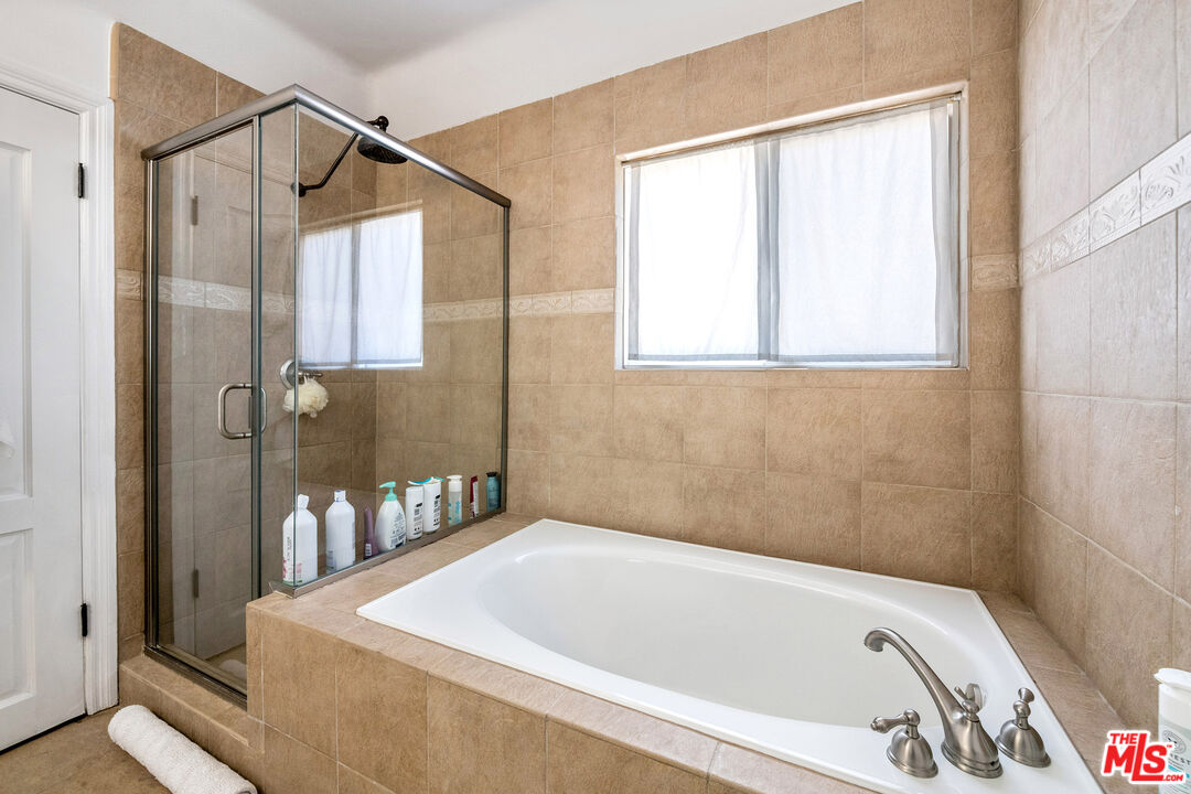 Tiled bathroom with a built-in soaking tub, glass shower enclosure, and curtained window.