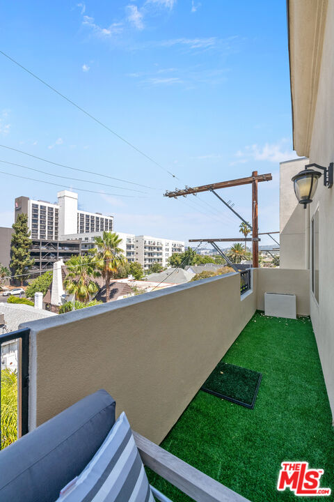 Apartment balcony with artificial turf and a view of nearby buildings and palm trees.