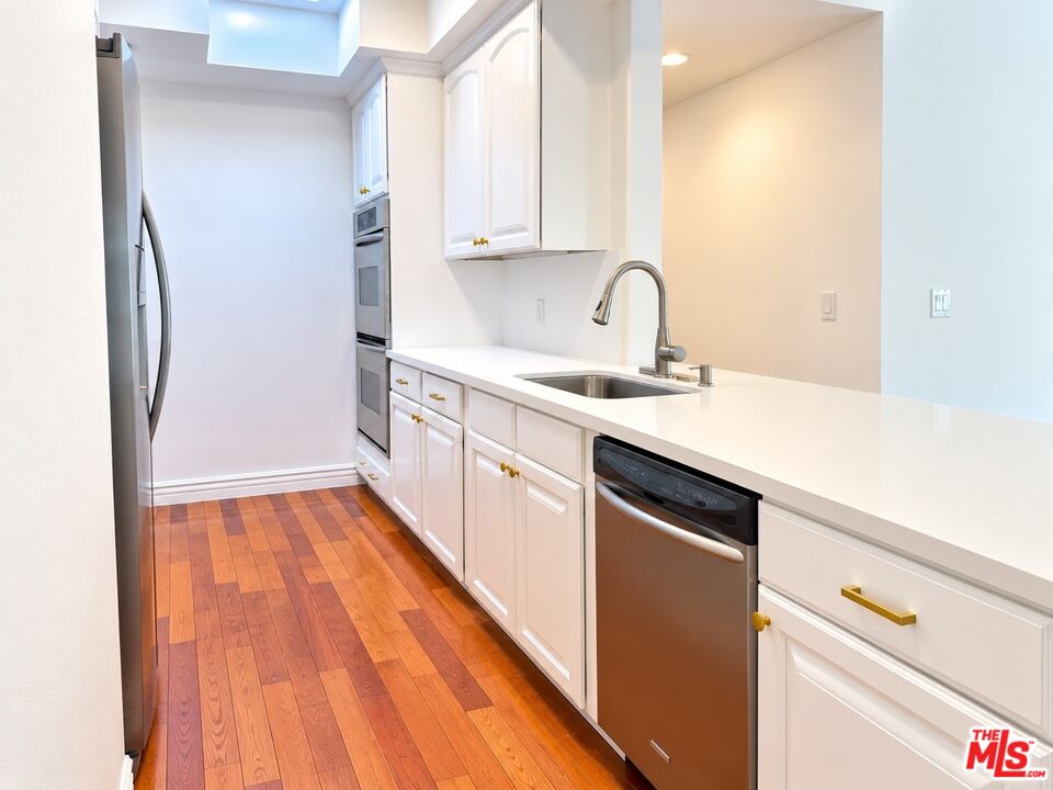 Modern kitchen with white cabinets, stainless-steel appliances, and warm hardwood floors.