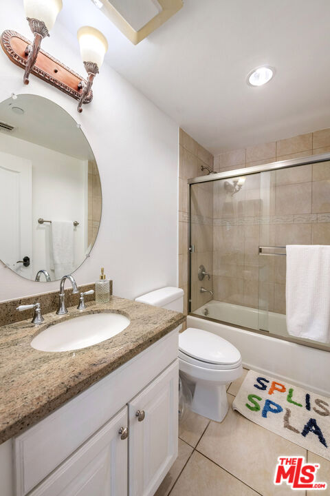 Bathroom with a granite vanity, oval sink, toilet, and glass-enclosed tiled bathtub.