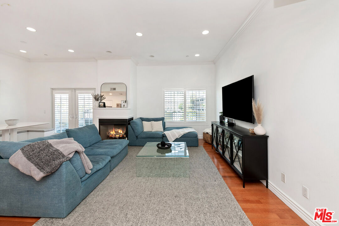 Staged living room with blue sectional sofas, a glass coffee table, and a lit fireplace.