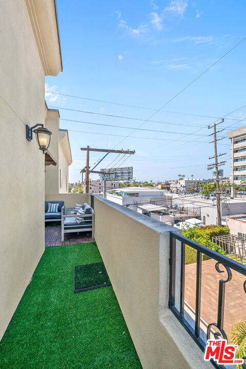 Apartment balcony with artificial turf and seating overlooking an urban neighborhood.
