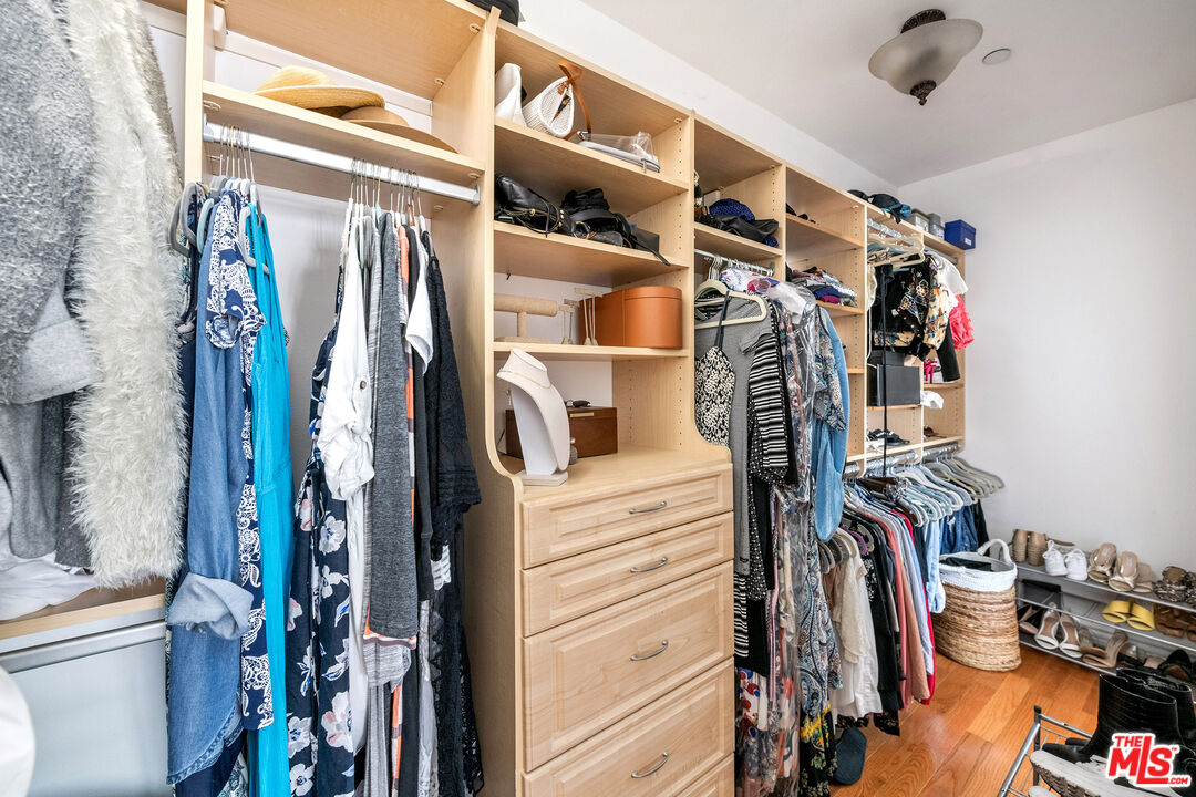 Walk-in closet with built-in wood shelving and drawers, packed with hanging clothes and shoes.