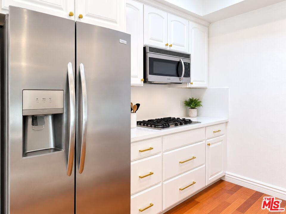 White kitchen with stainless steel refrigerator, gas cooktop, built-in microwave, and gold cabinet hardware.