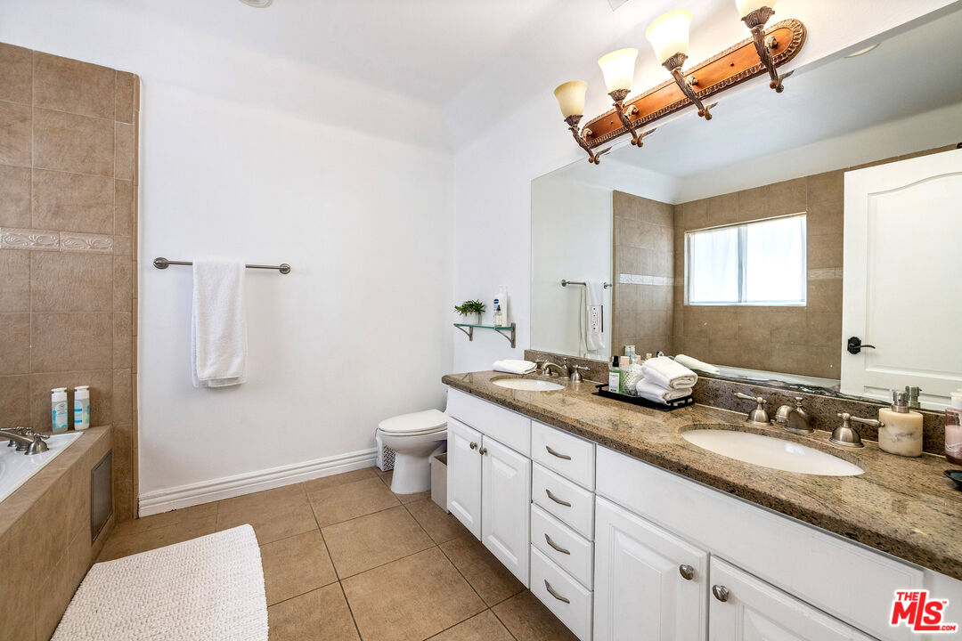 Bathroom with a granite double-sink vanity, large mirror, and tan tiled bathtub surround.