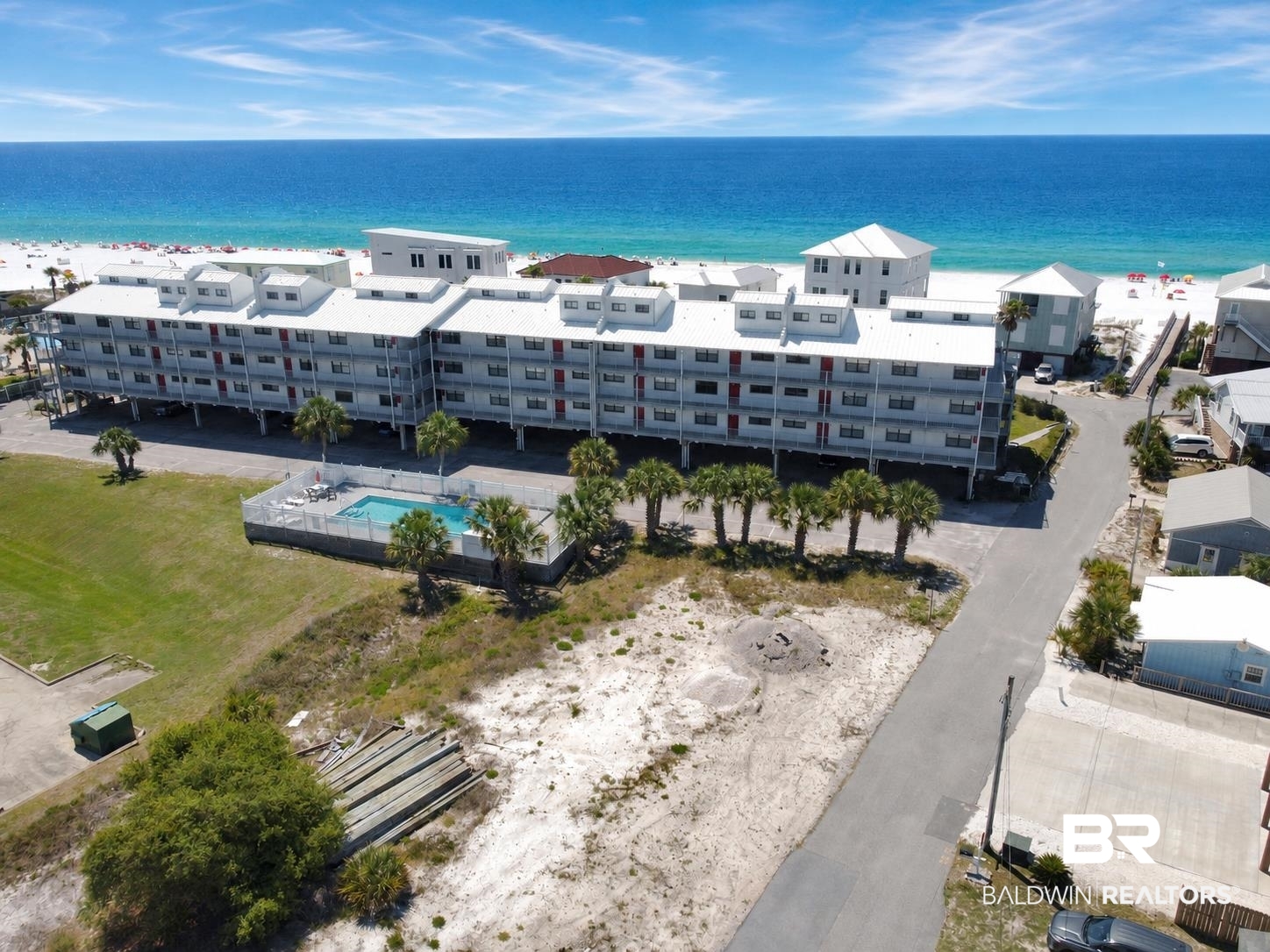 Beachfront condominium complex with a fenced pool, palm trees, and Gulf waters beyond.