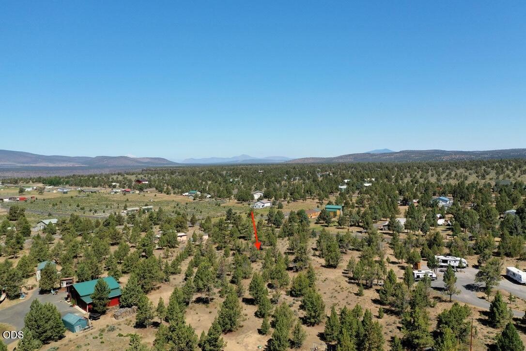 Aerial view of a tree-covered rural parcel marked by a red arrow, with scattered homes and distant hills.