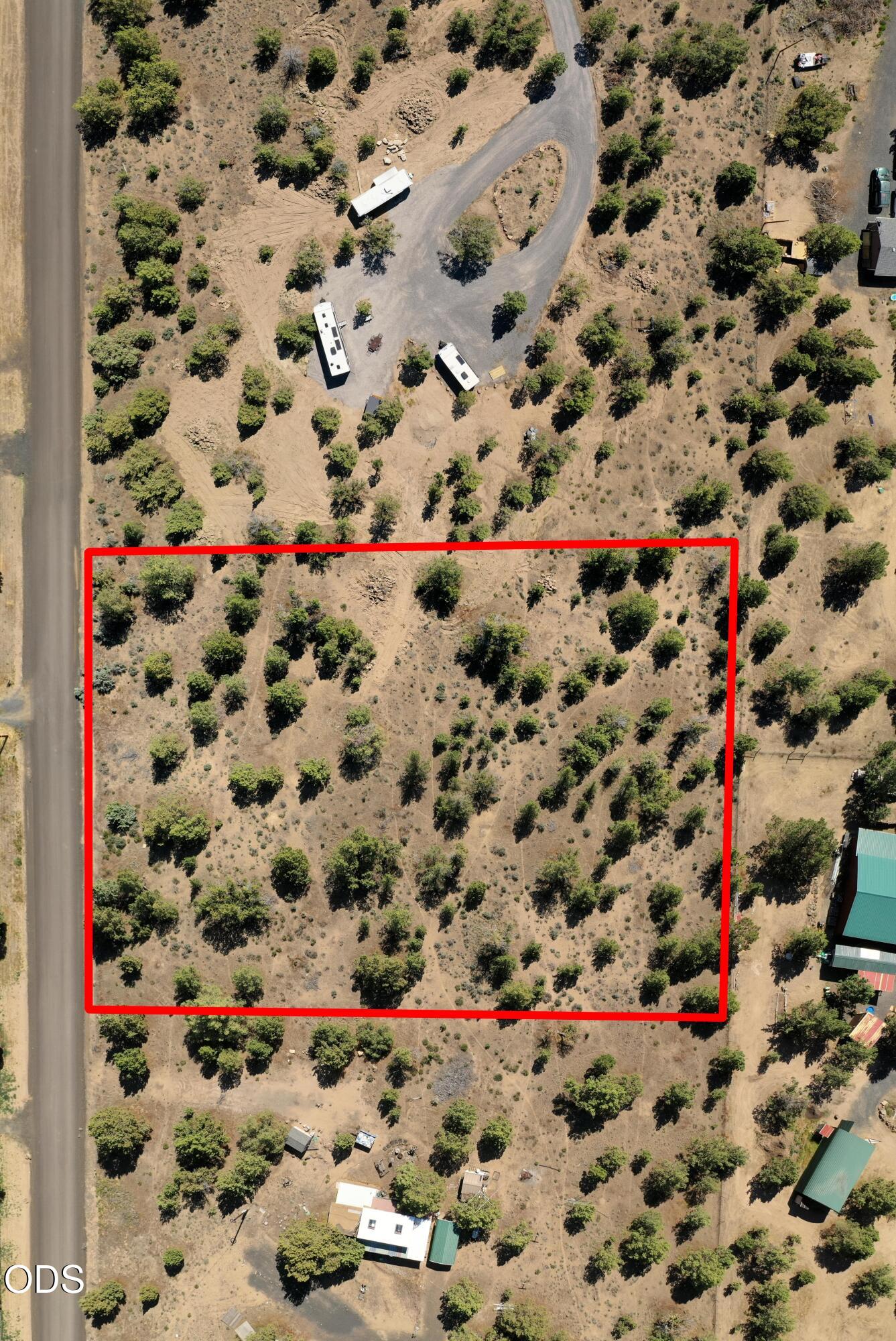Aerial view of a sparsely treed parcel outlined in red beside a road.
