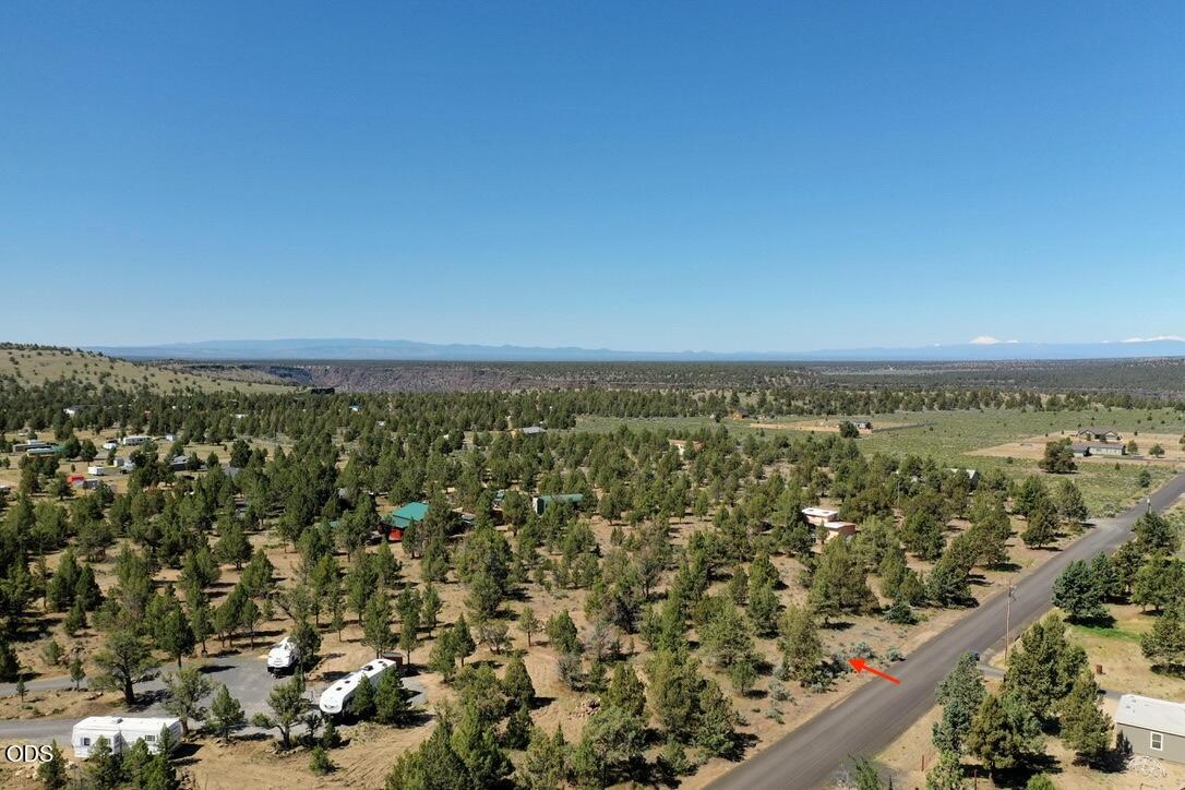 Aerial view of rural land with scattered trees, homes, a road, and distant mountains; a red arrow marks the roadside.