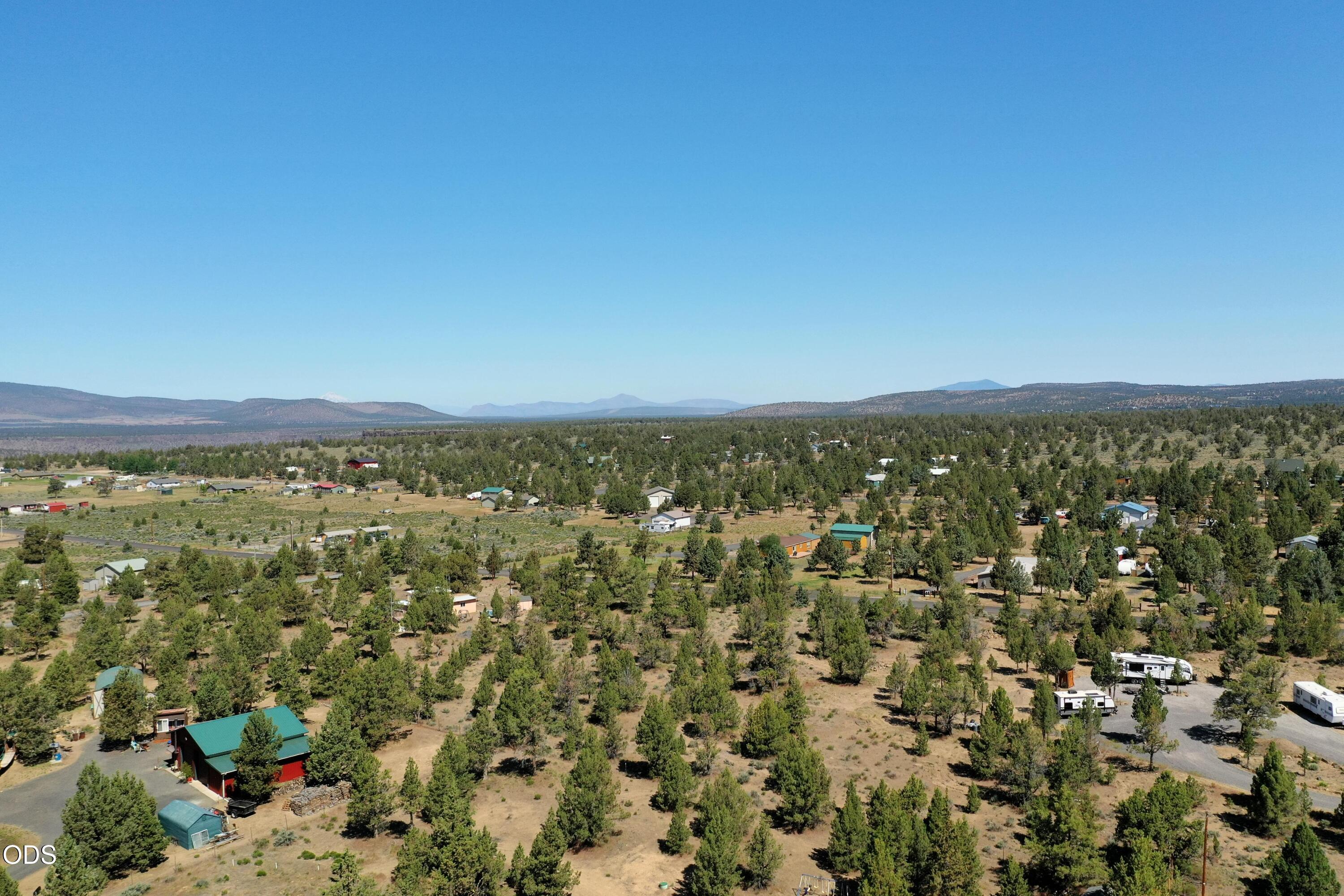 Aerial view of rural land with scattered homes, pine trees, and distant mountains.