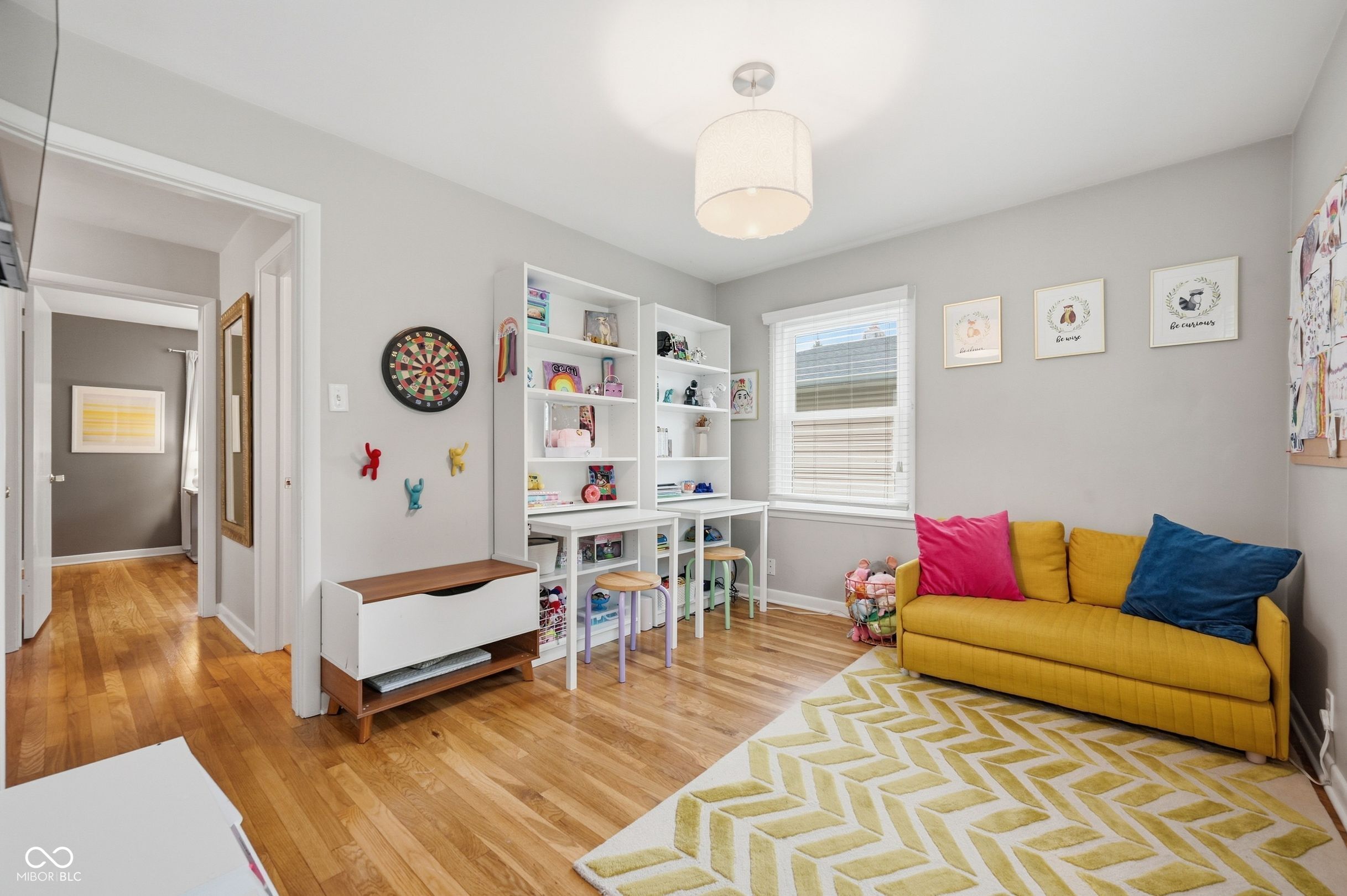 Children’s playroom with white shelving, a yellow sofa, dartboard, and geometric rug.