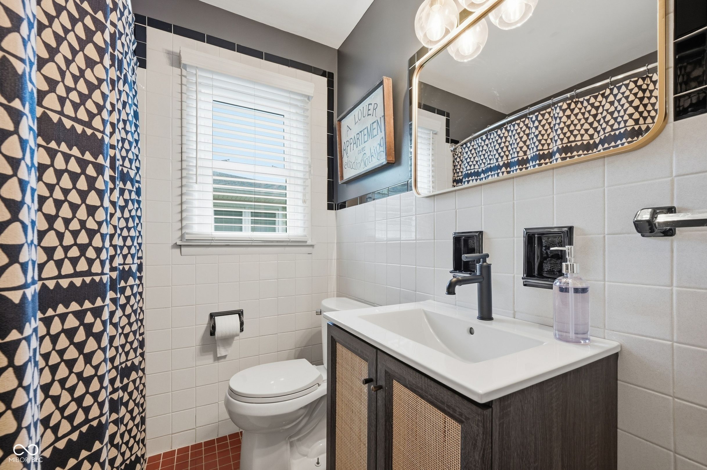 Bathroom with a dark wood vanity, black fixtures, white tile, and a geometric shower curtain.