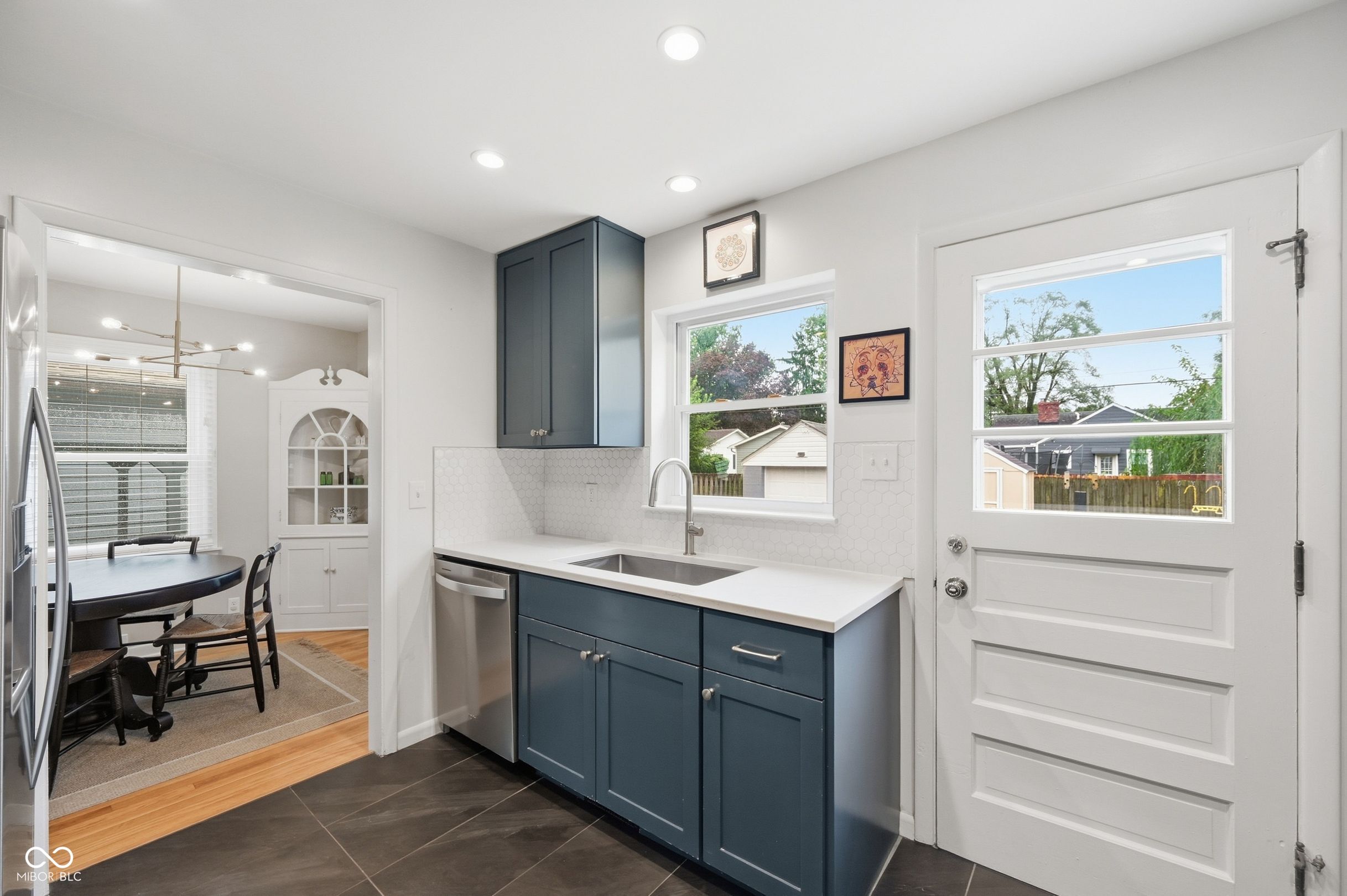 Kitchen with dark blue cabinets, white tile backsplash, and a windowed back door beside a dining nook.