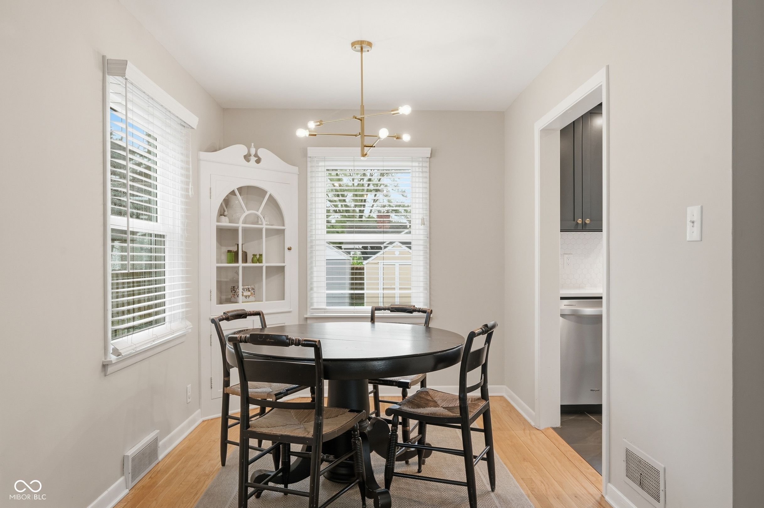 Dining room with a round table, built-in display cabinet, and brass chandelier beside the kitchen.