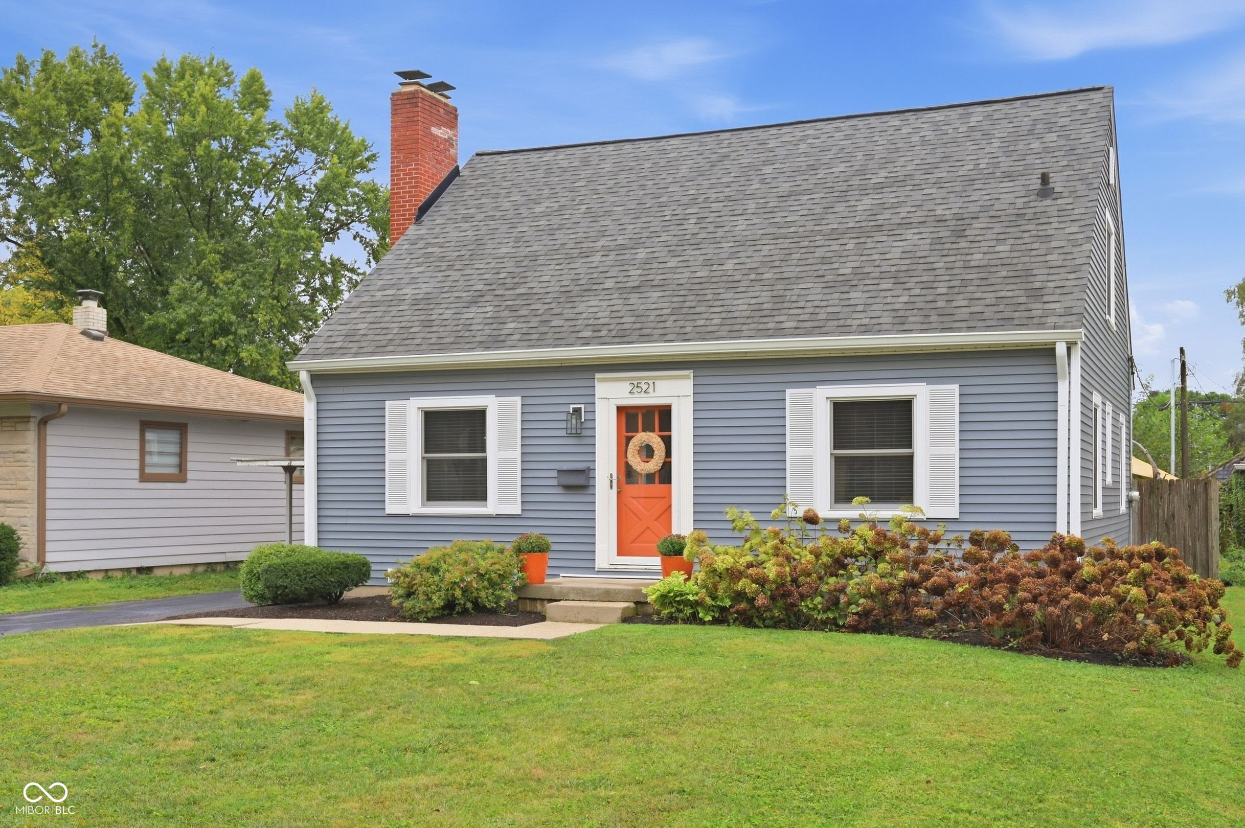 Blue-gray two-story house with white shutters, orange front door, and landscaped front garden.