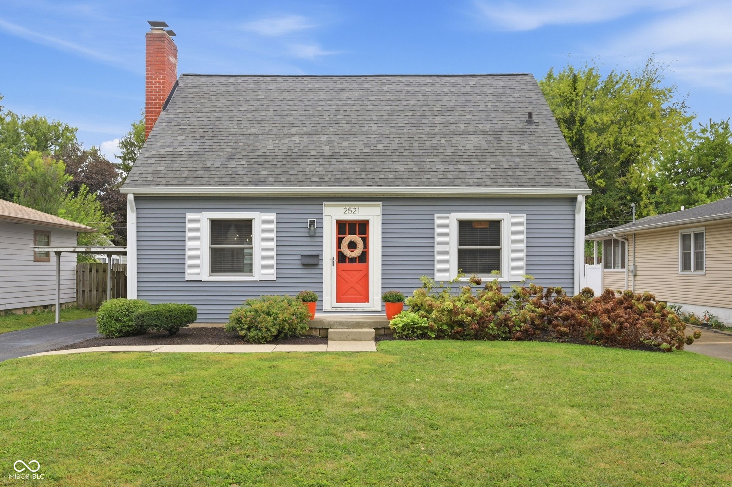 Blue-gray house with a red front door, white shutters, and landscaped lawn.