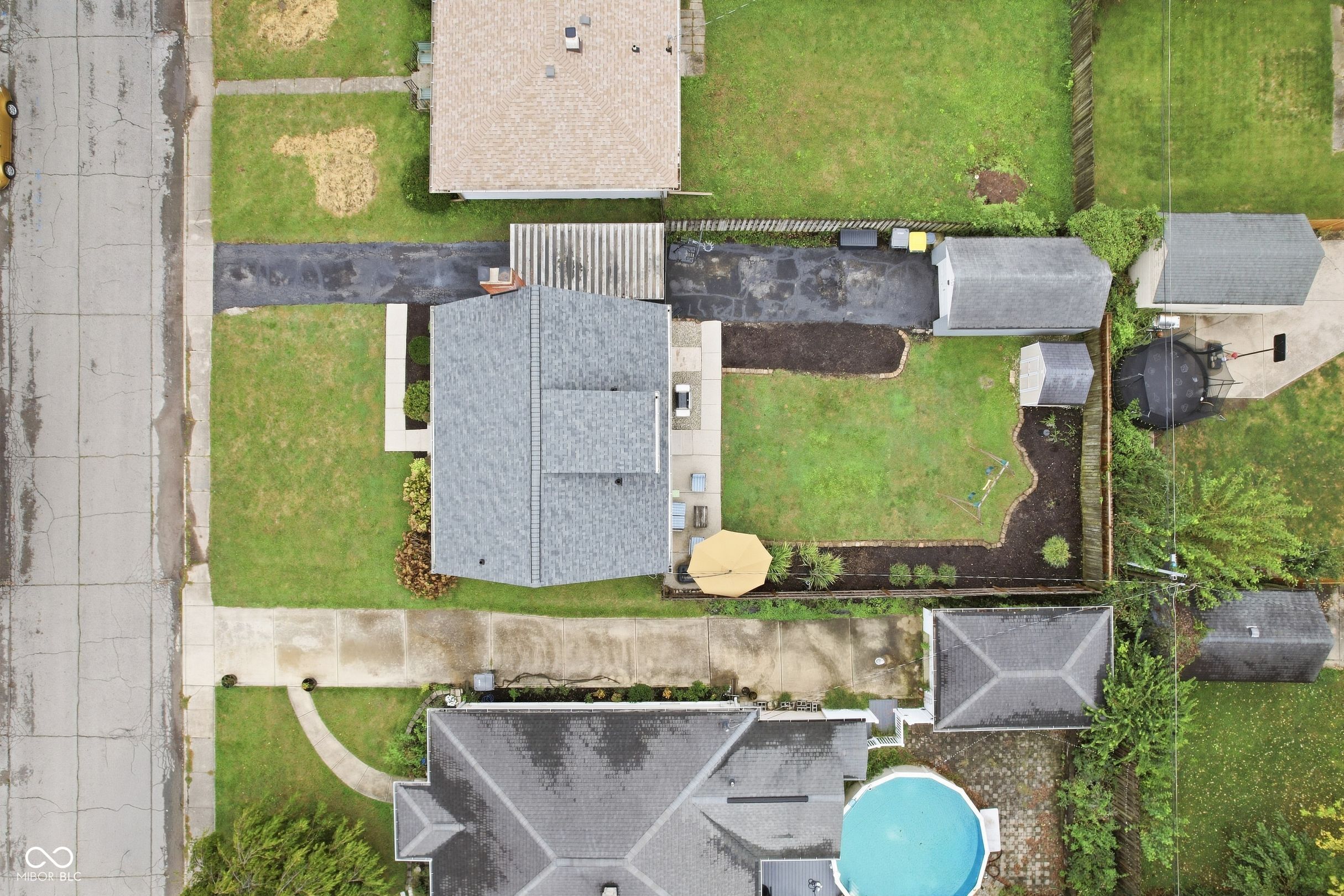 Aerial view of a gray-roofed house with a fenced yard and landscaped garden beds.