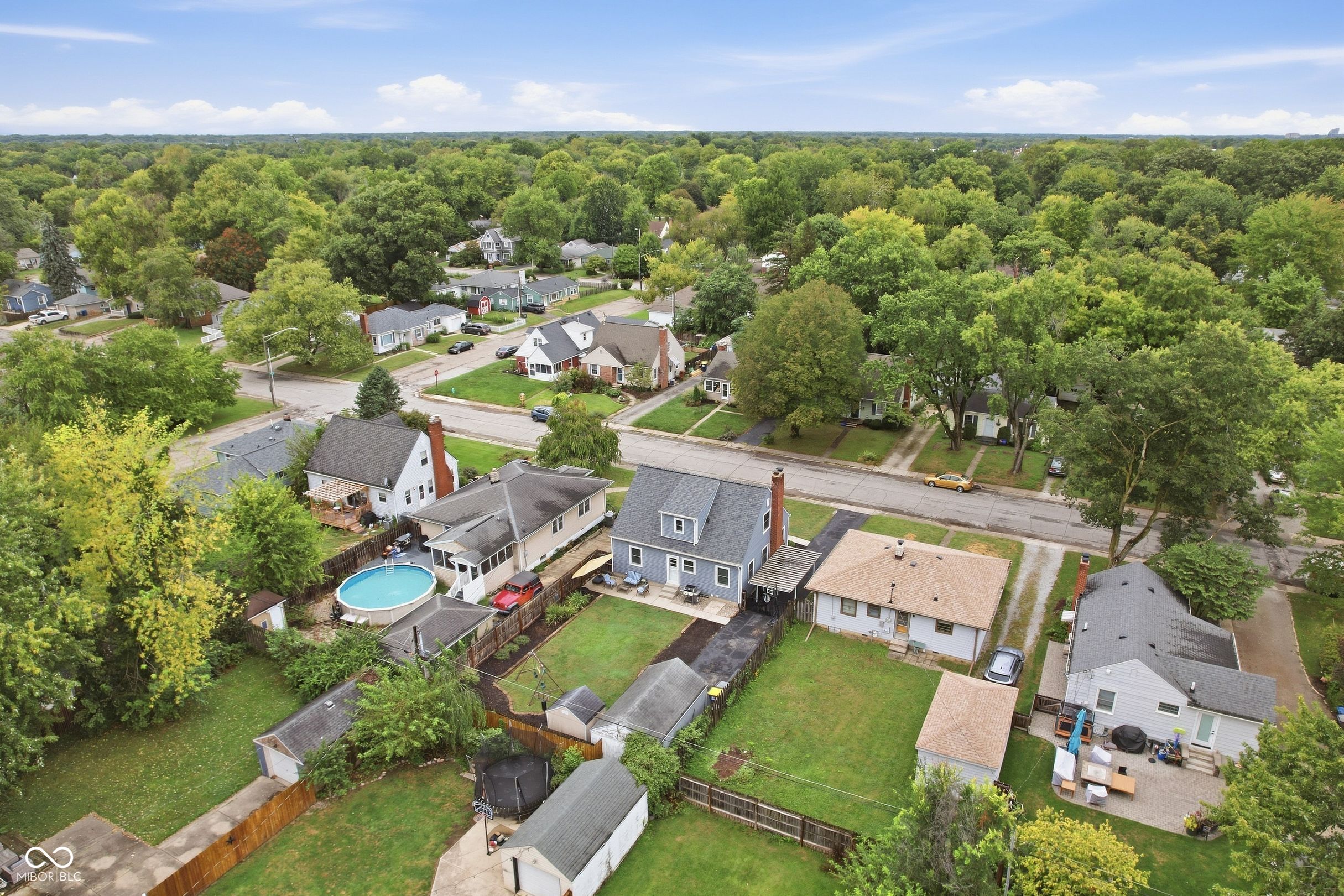Aerial view of a blue two-story house with a fenced lawn among tree-lined Indianapolis streets.